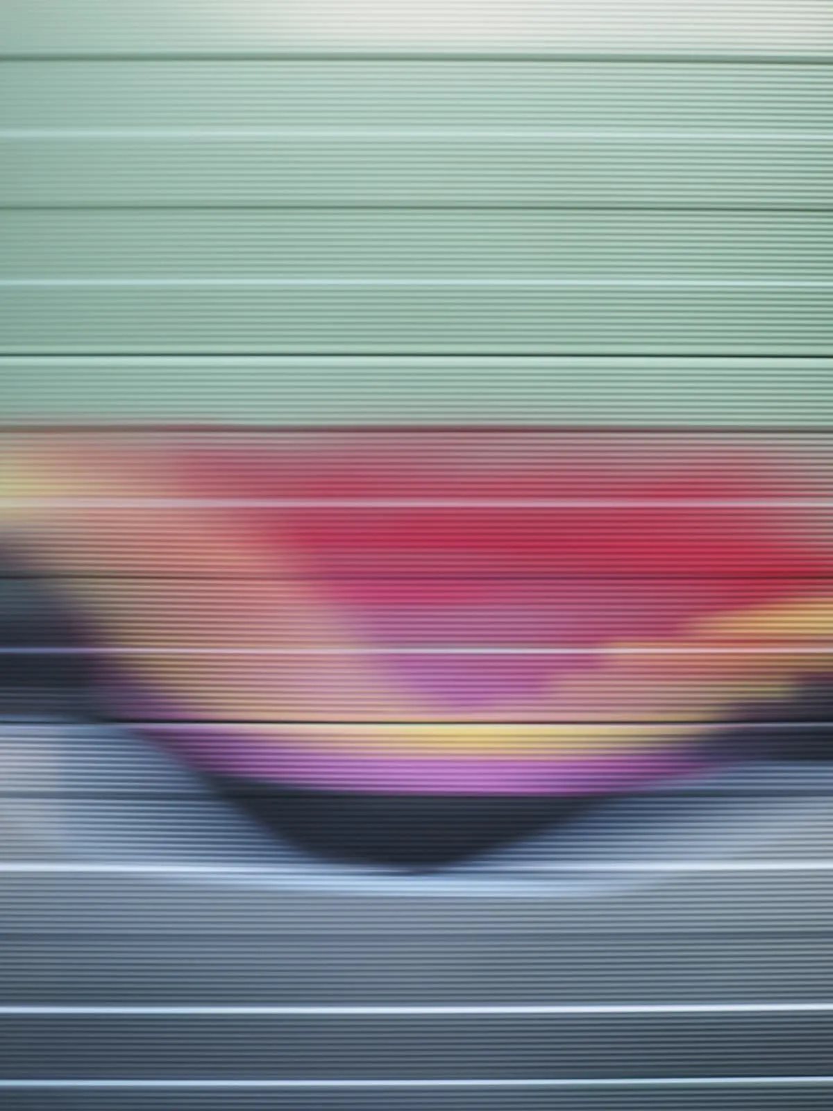Motion blur of a red and yellow shape on a green slatted wall, 2026