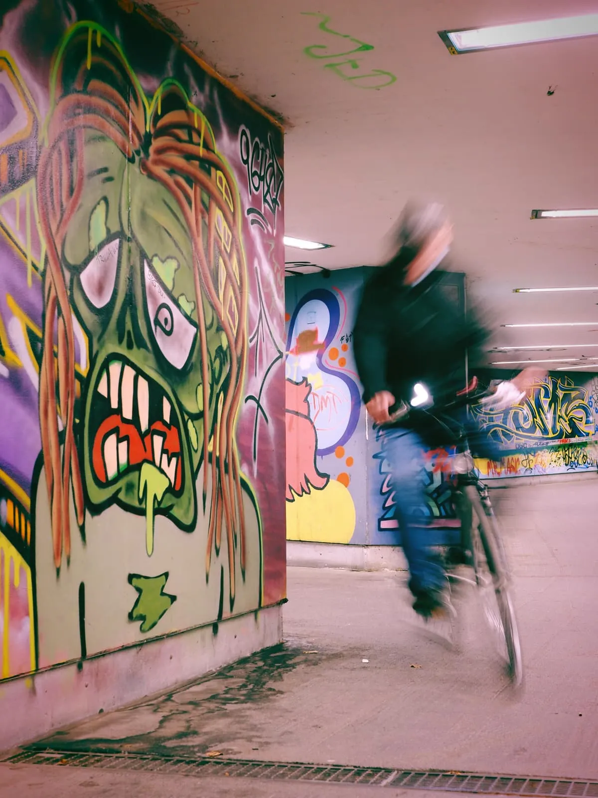 Blurred cyclist passing a mural of a green monster, 2021