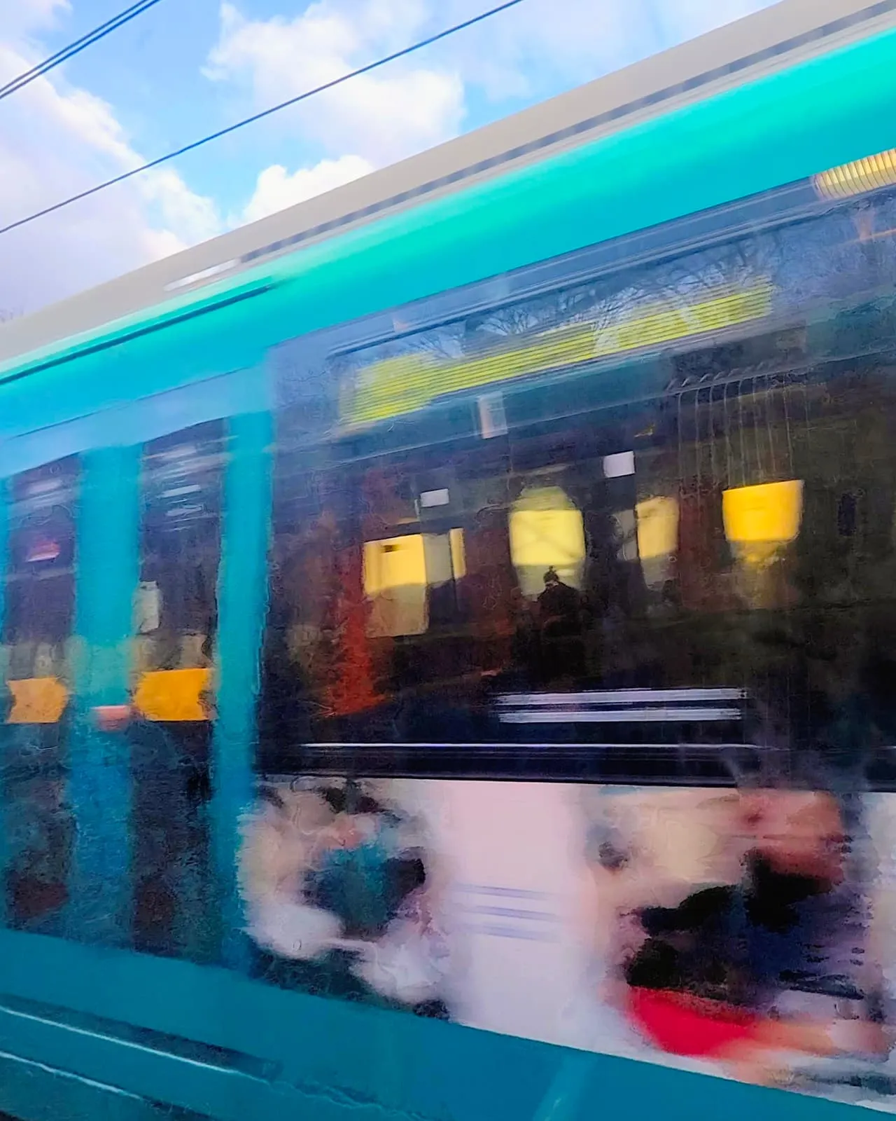 Turquoise tram streaked by motion under a blue sky, 2025