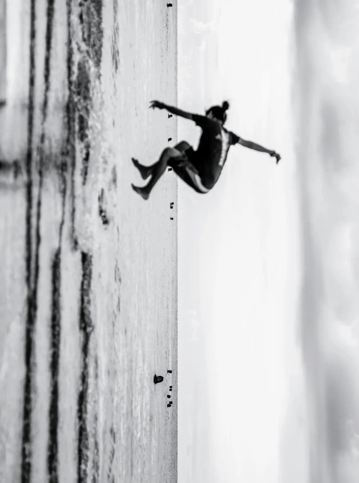 Black and white, a figure falling sideways across a pale field, 2022