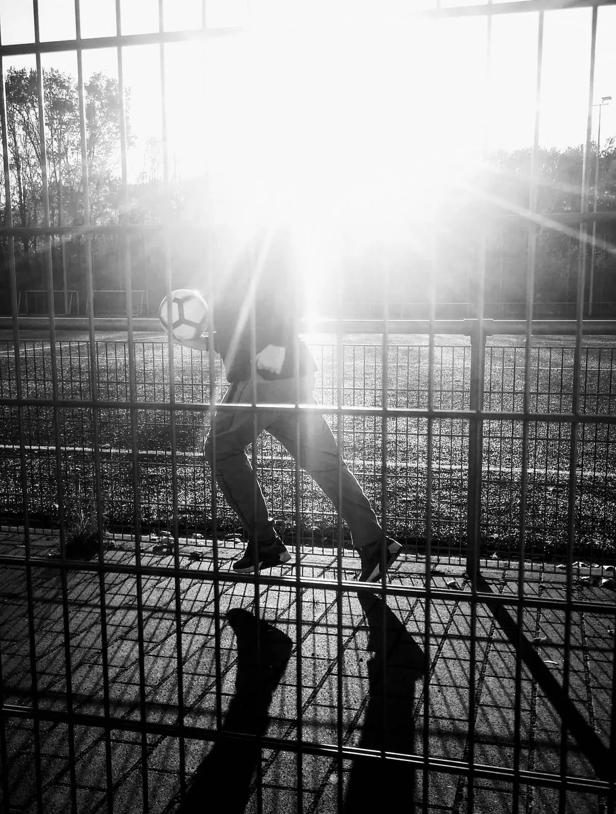 Black and white, a player with a ball behind a fence against the sun, 2018