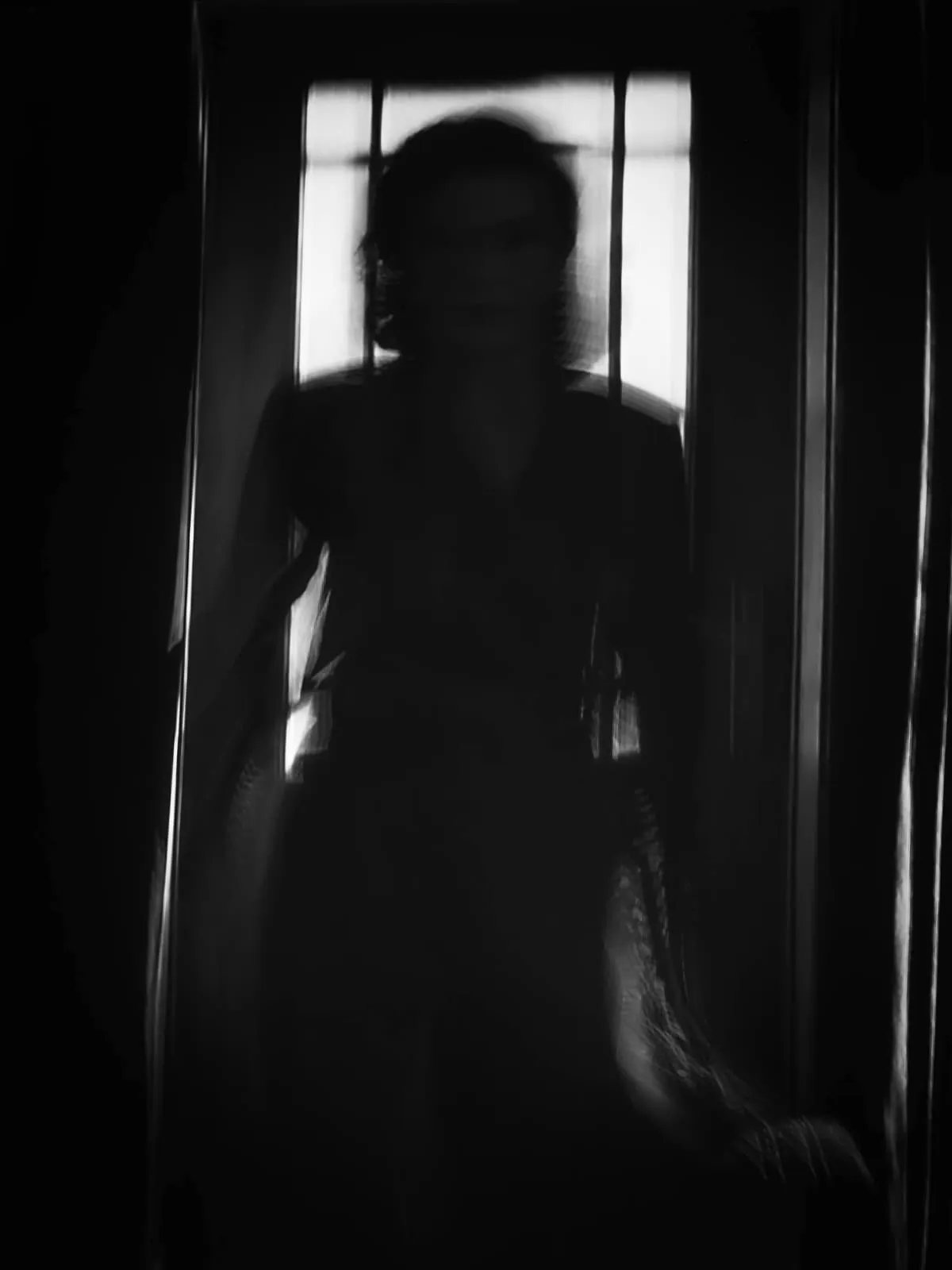Black and white dark figure in front of a dim window, 2020