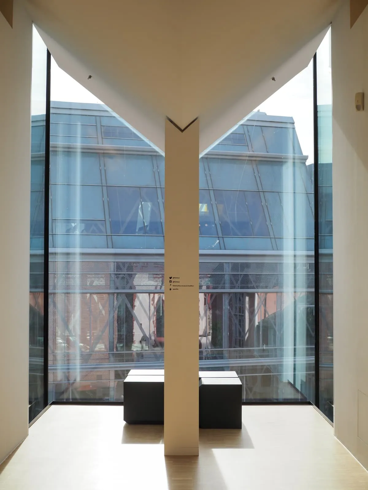 V shaped white column in front of a glass wall, 2026