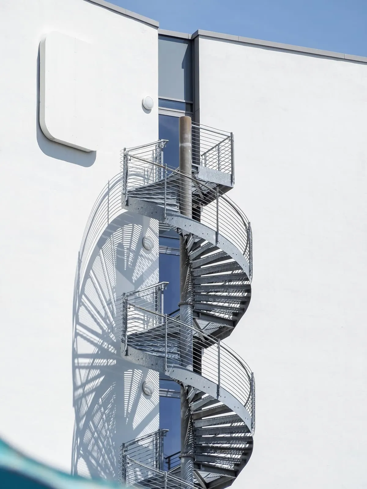 Steel spiral stair and its shadow on a white facade, 2020