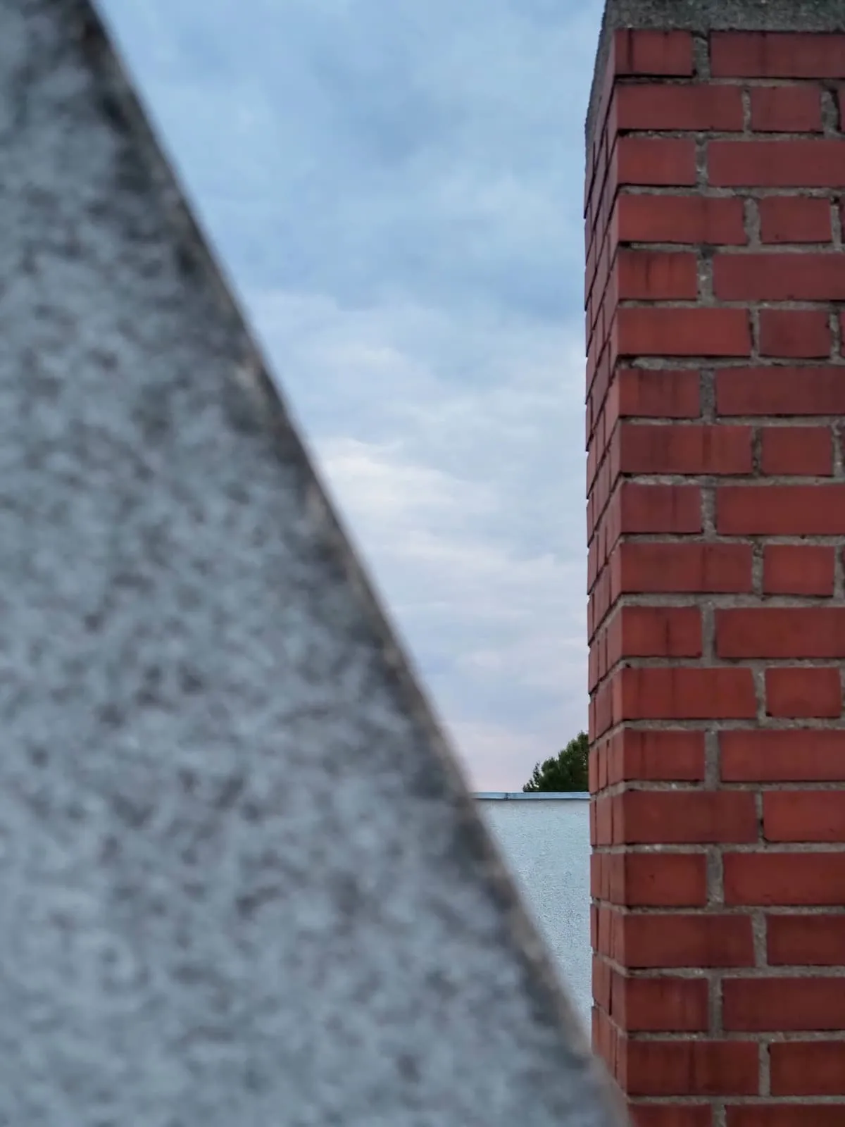 Blurred grey gable edge and a brick chimney, sky between, 2020