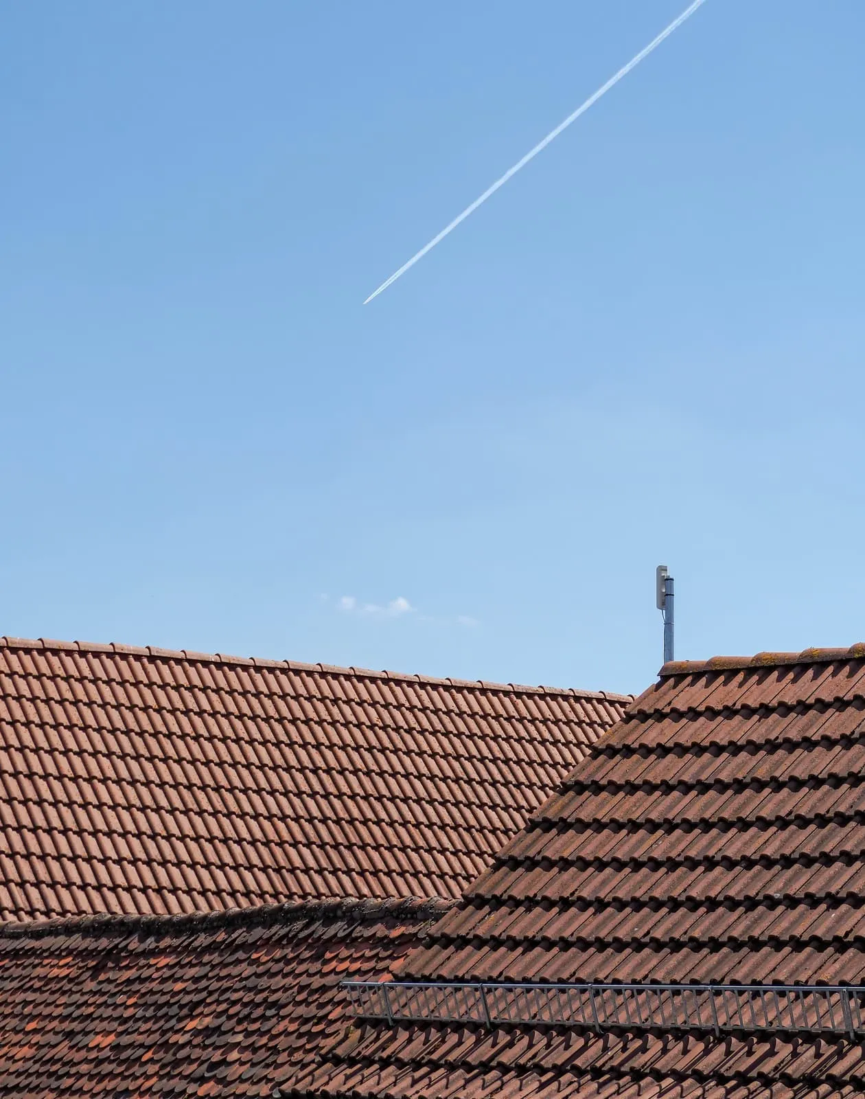 Tiled roofs low in the frame, a contrail in the empty sky, 2020