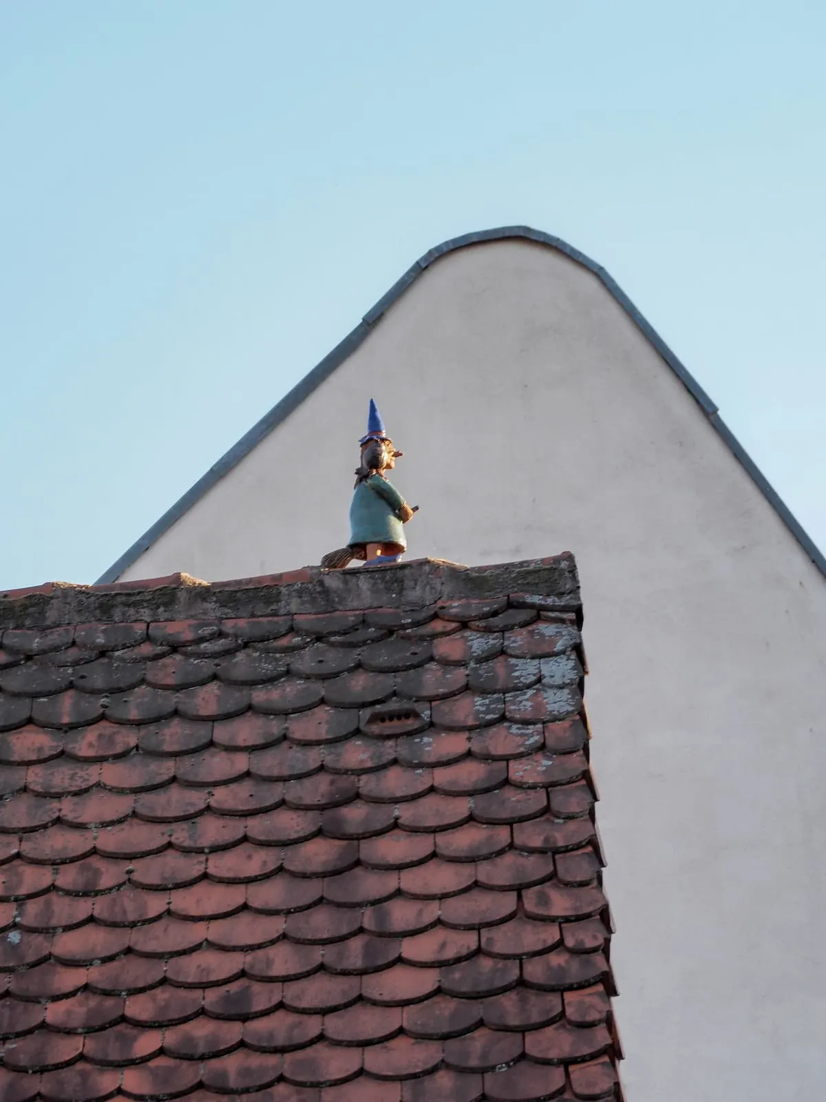 A garden gnome standing on a roof ridge below a rounded gable, 2020