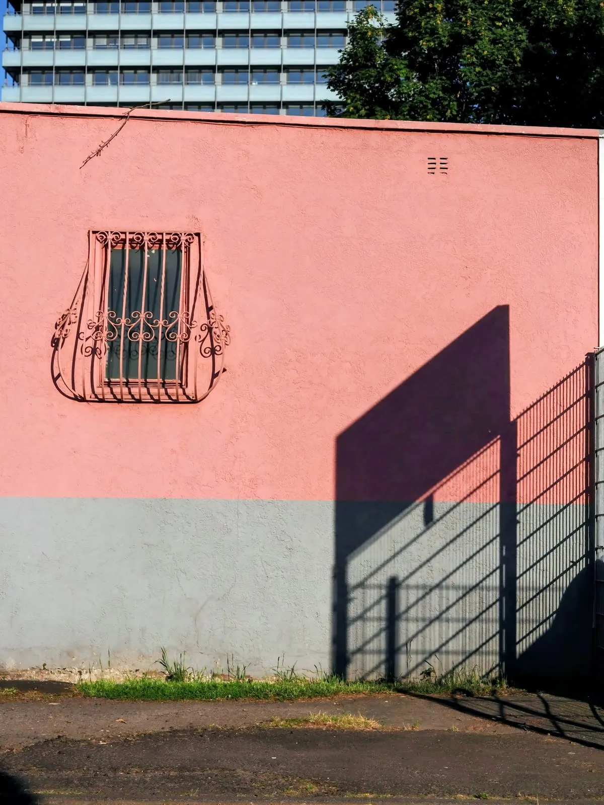 Pink wall with a barred window and a sharp shadow, 2020