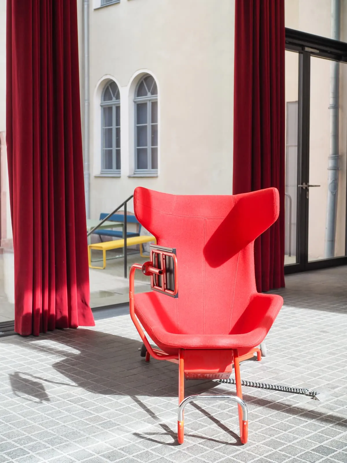 Red armchair on a tiled floor between red curtains, 2026