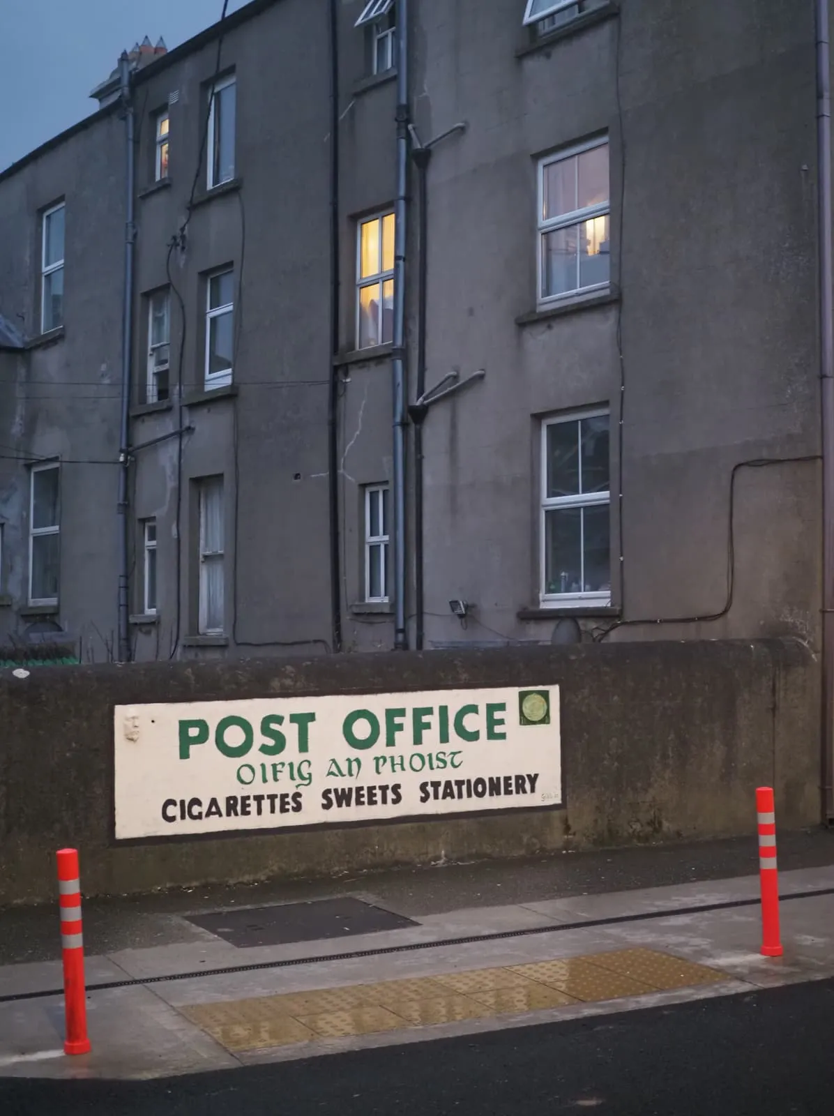 Post office sign on a wall below a grey tenement, 2026