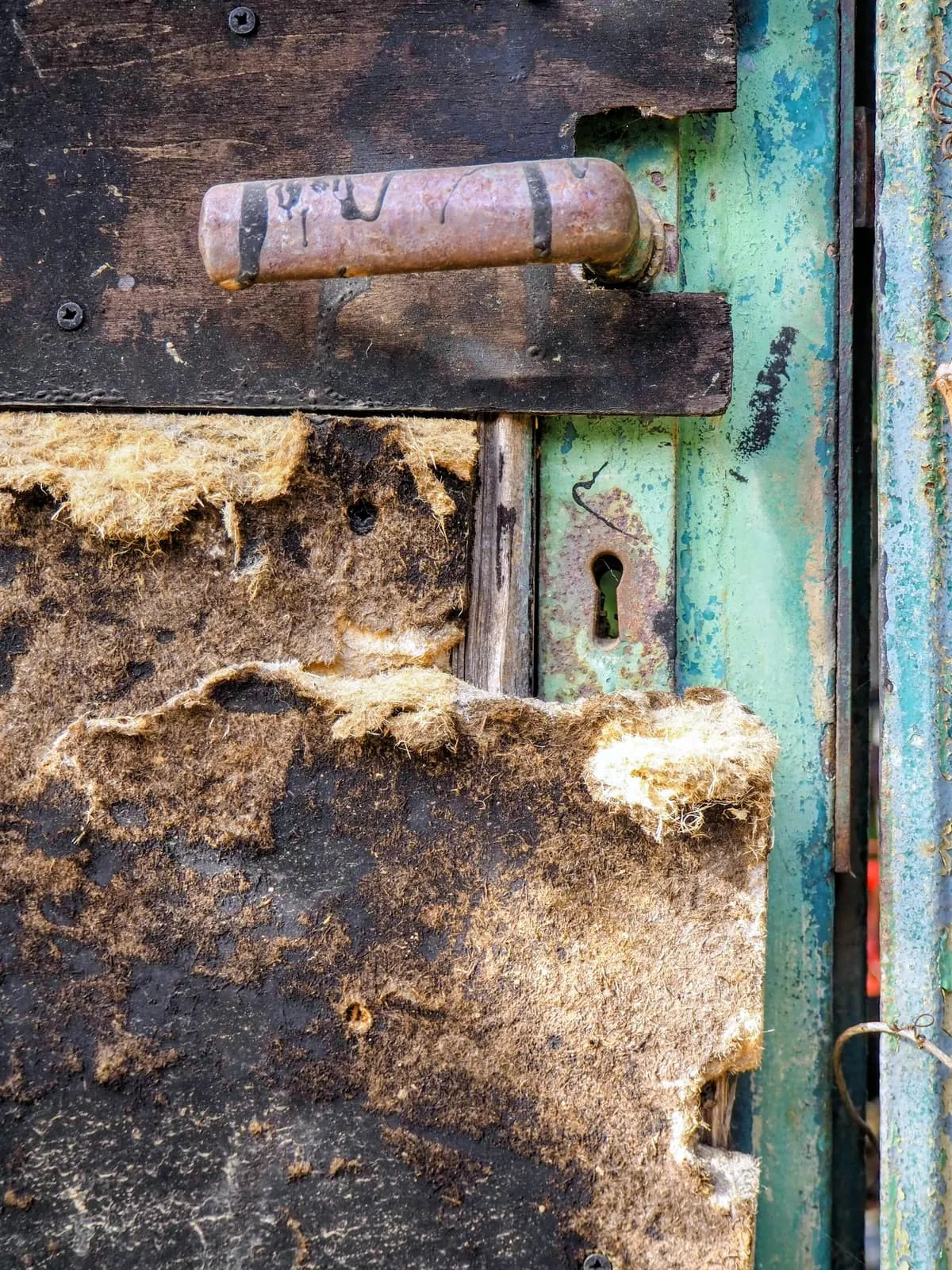 Rusted door handle and torn felt on a green door, 2021