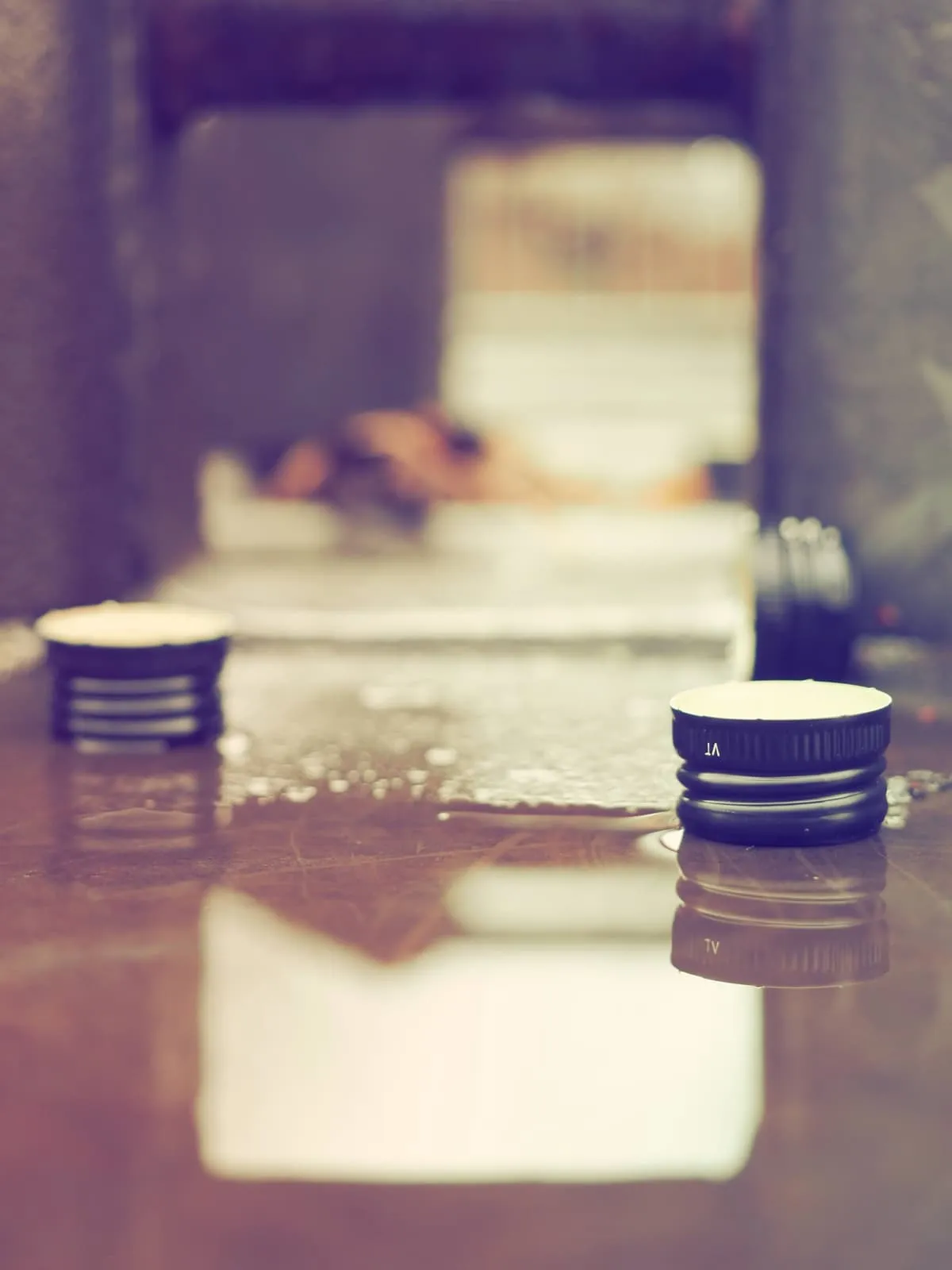 Two bottle caps on a wet table, out of focus beyond, 2021