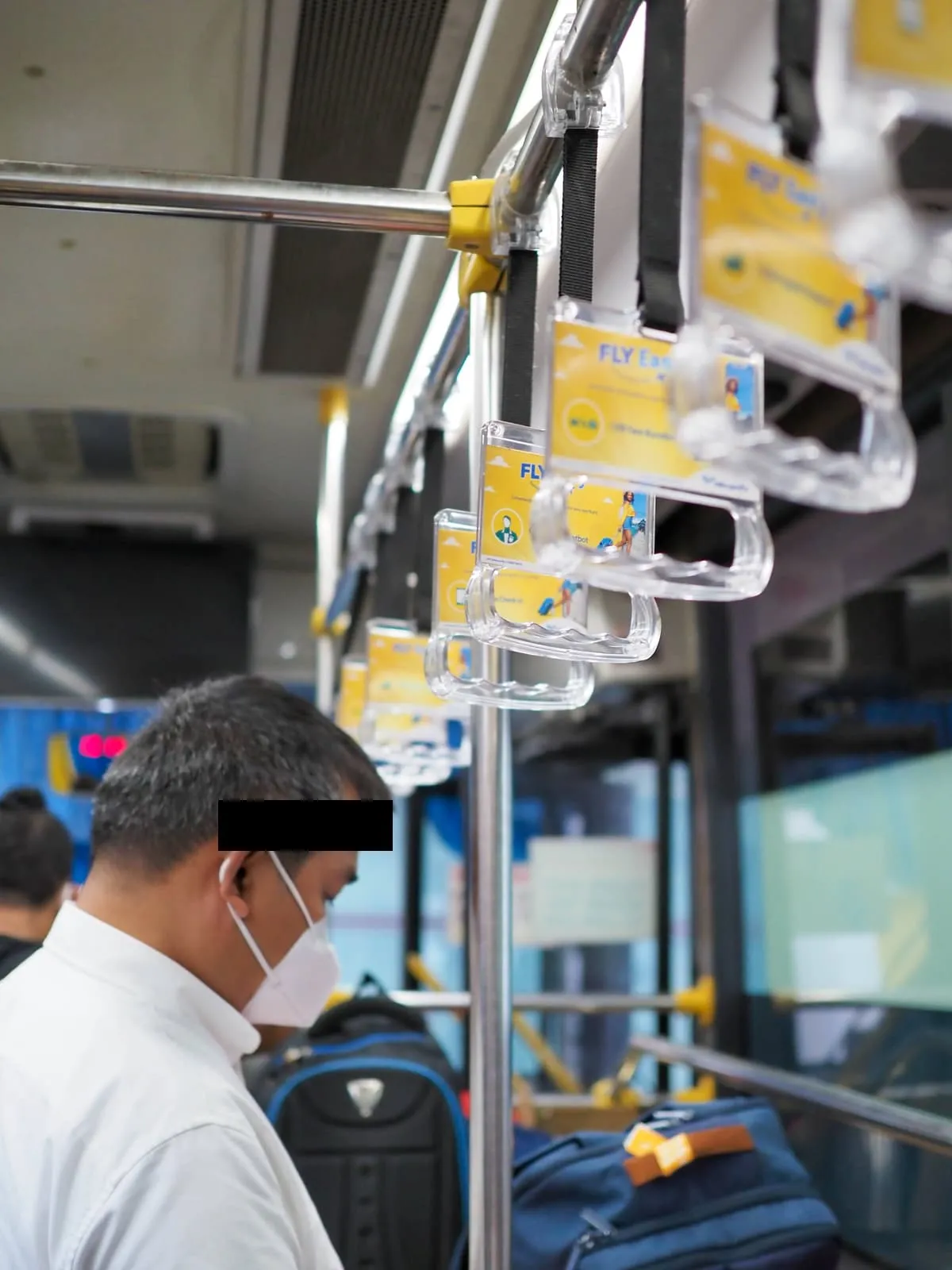 Man in a face mask on a bus under hanging grab handles, eyes barred, 2022
