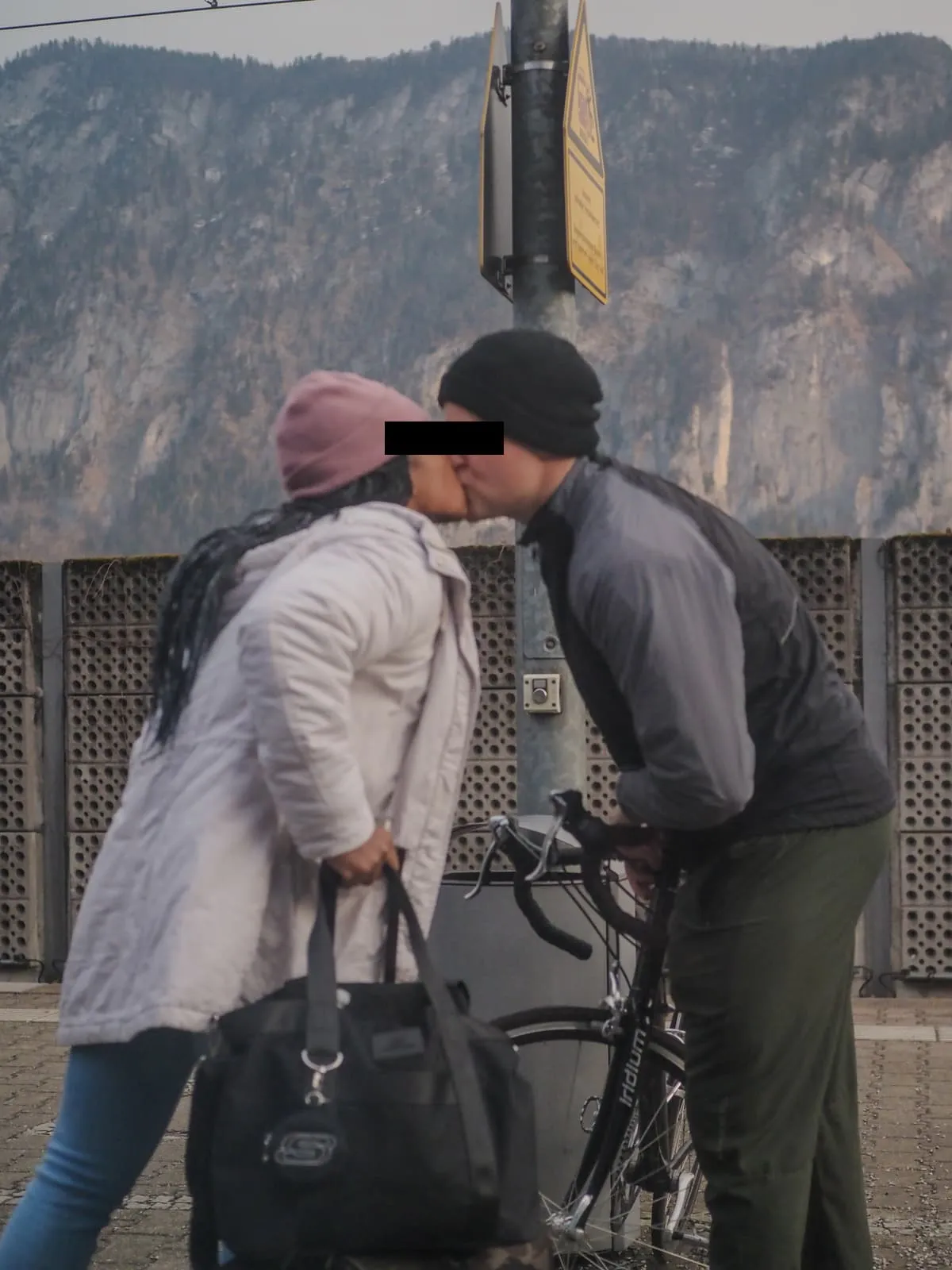 Two people kissing beside a bicycle, eyes barred, 2026
