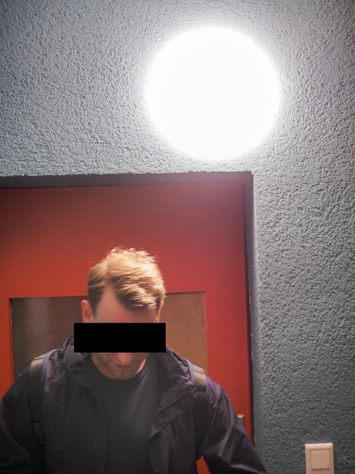 Man looking down under a round lamp, eyes barred, 2026