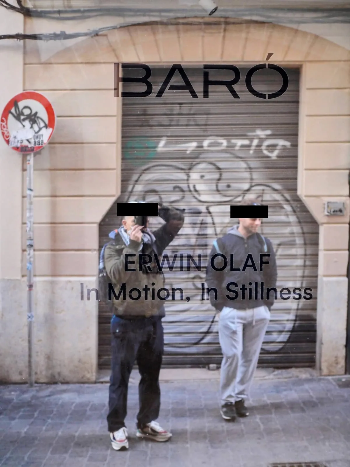 Photographer and a man reflected in a shop window, eyes barred, 2024