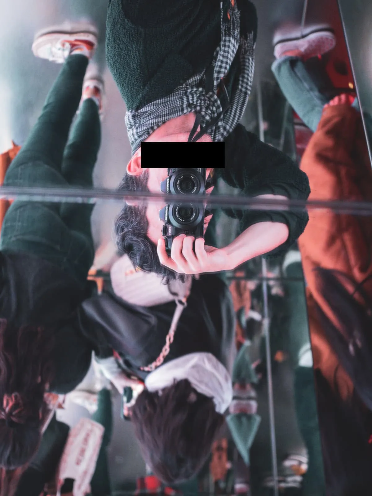 Upside down mirror view of a photographer among hanging shoes, eyes barred, 2024