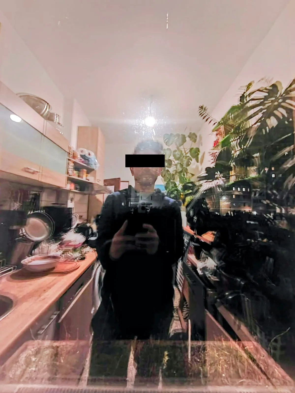 Blurred mirror view of a figure in a kitchen, eyes barred, 2025
