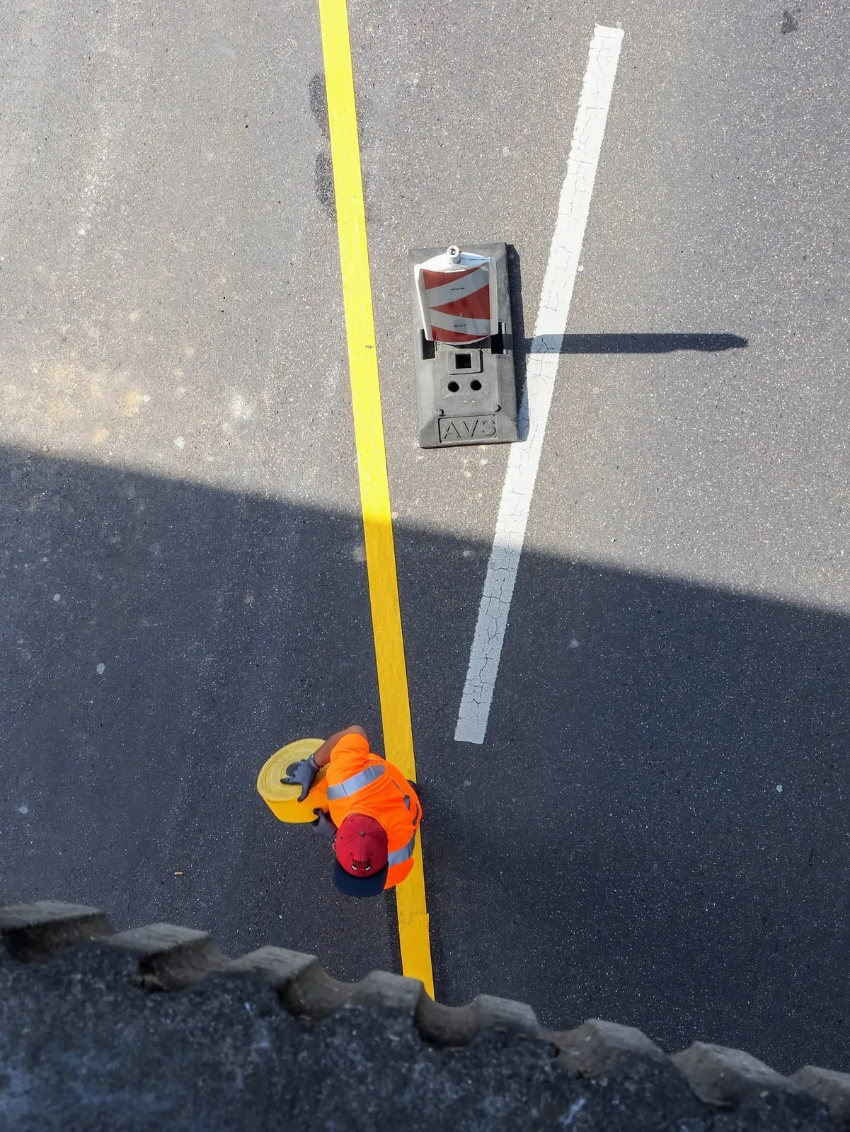 From above: road worker in orange beside a yellow line and a bollard, 2020