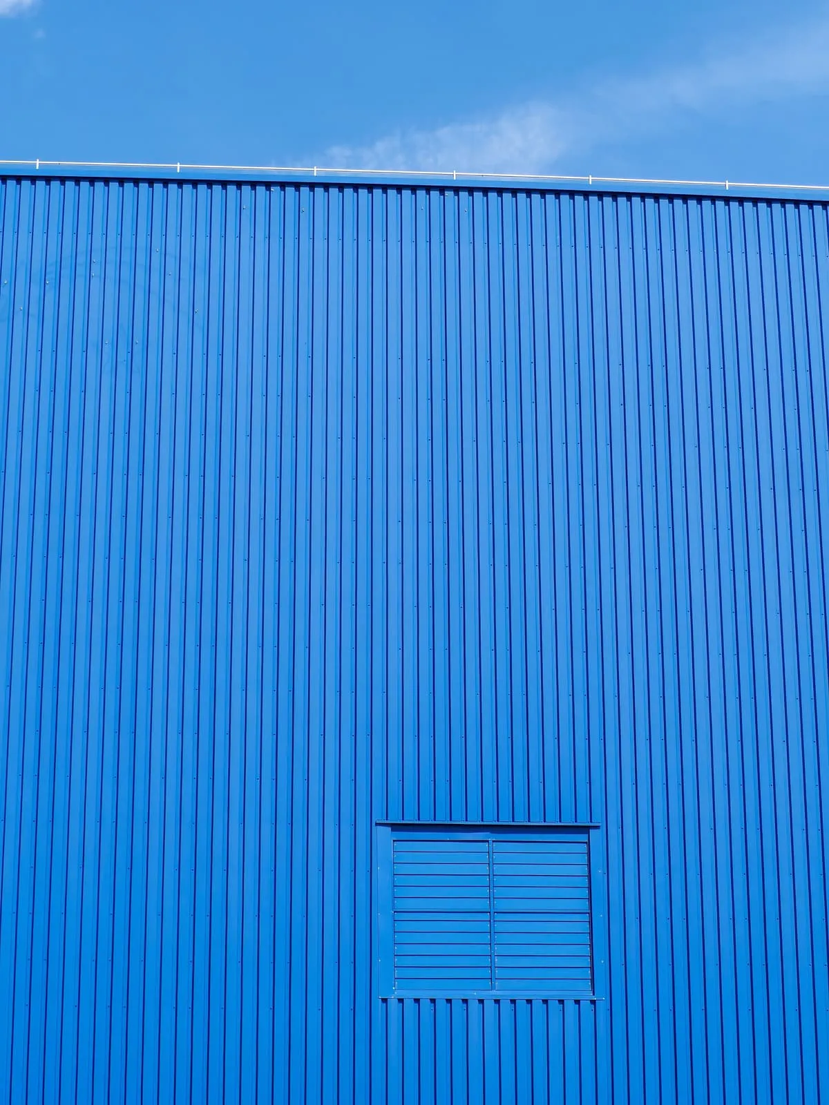 Blue corrugated wall with a vent, a strip of sky, 2020