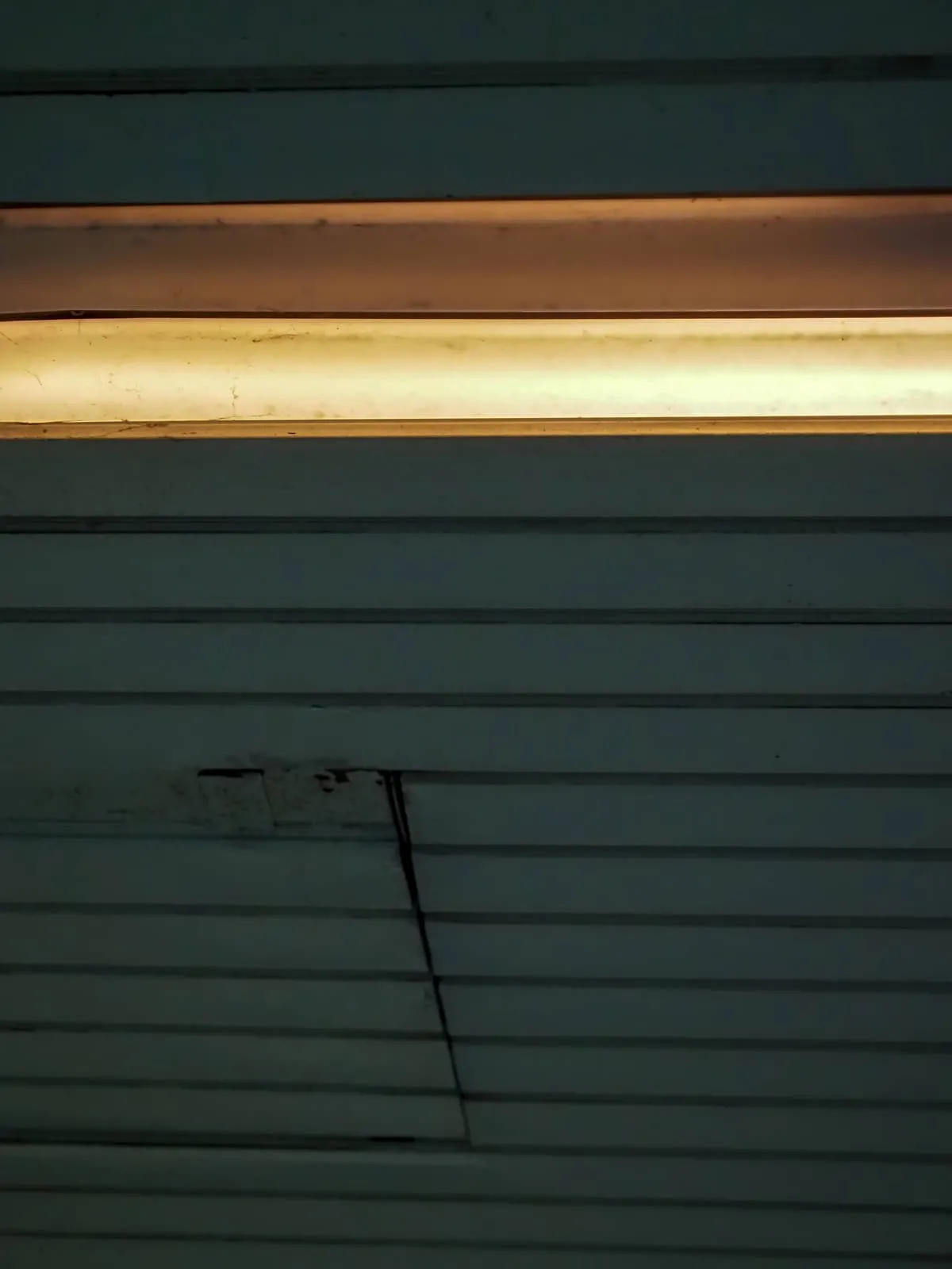 The lit strip again, higher, a crack in the slats, 2020