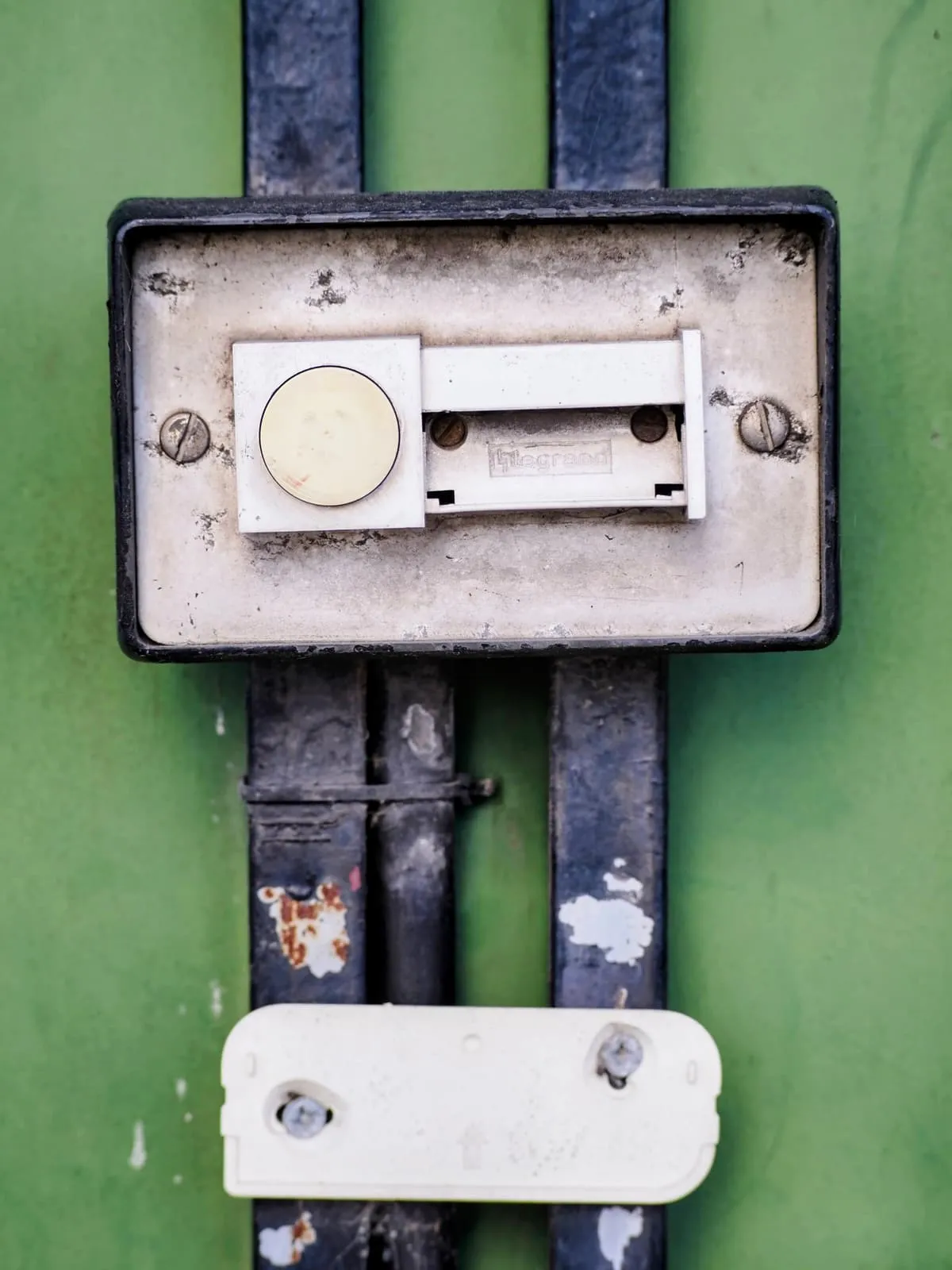 Old switch plate on green metal, two screws like eyes, 2025