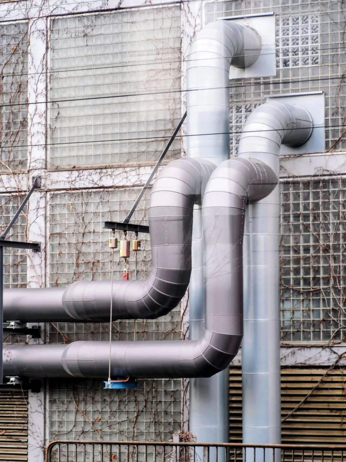 Two bent ventilation pipes on a wall of glass bricks, 2025