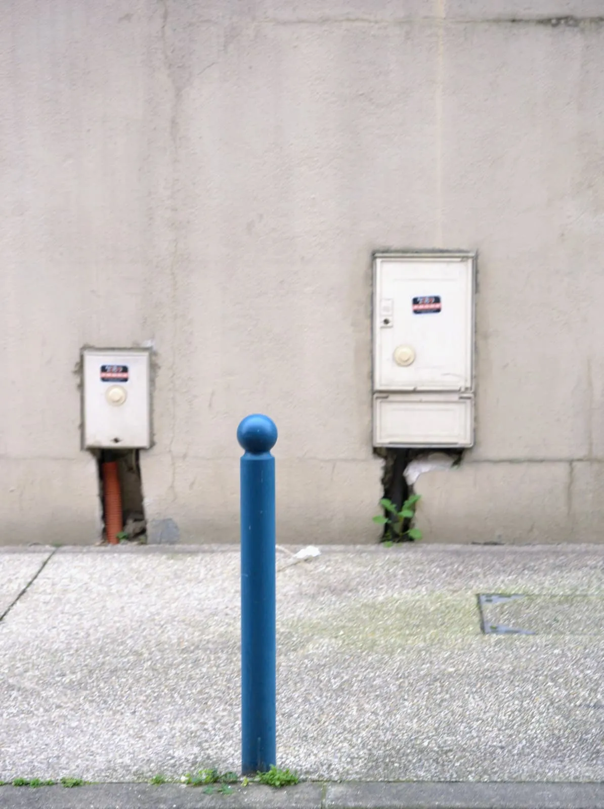Blue bollard on a pavement between two wall boxes, 2025