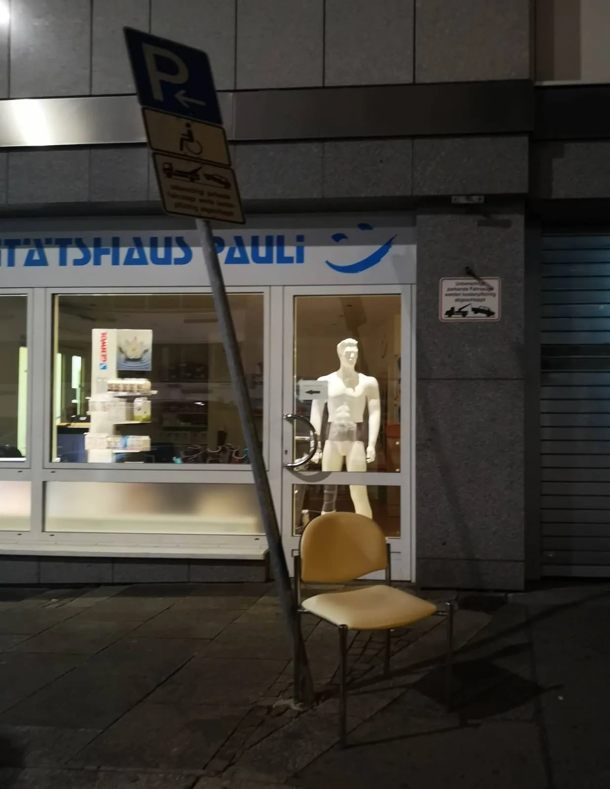 Headless mannequin in a shop window at night, a chair outside, 2018