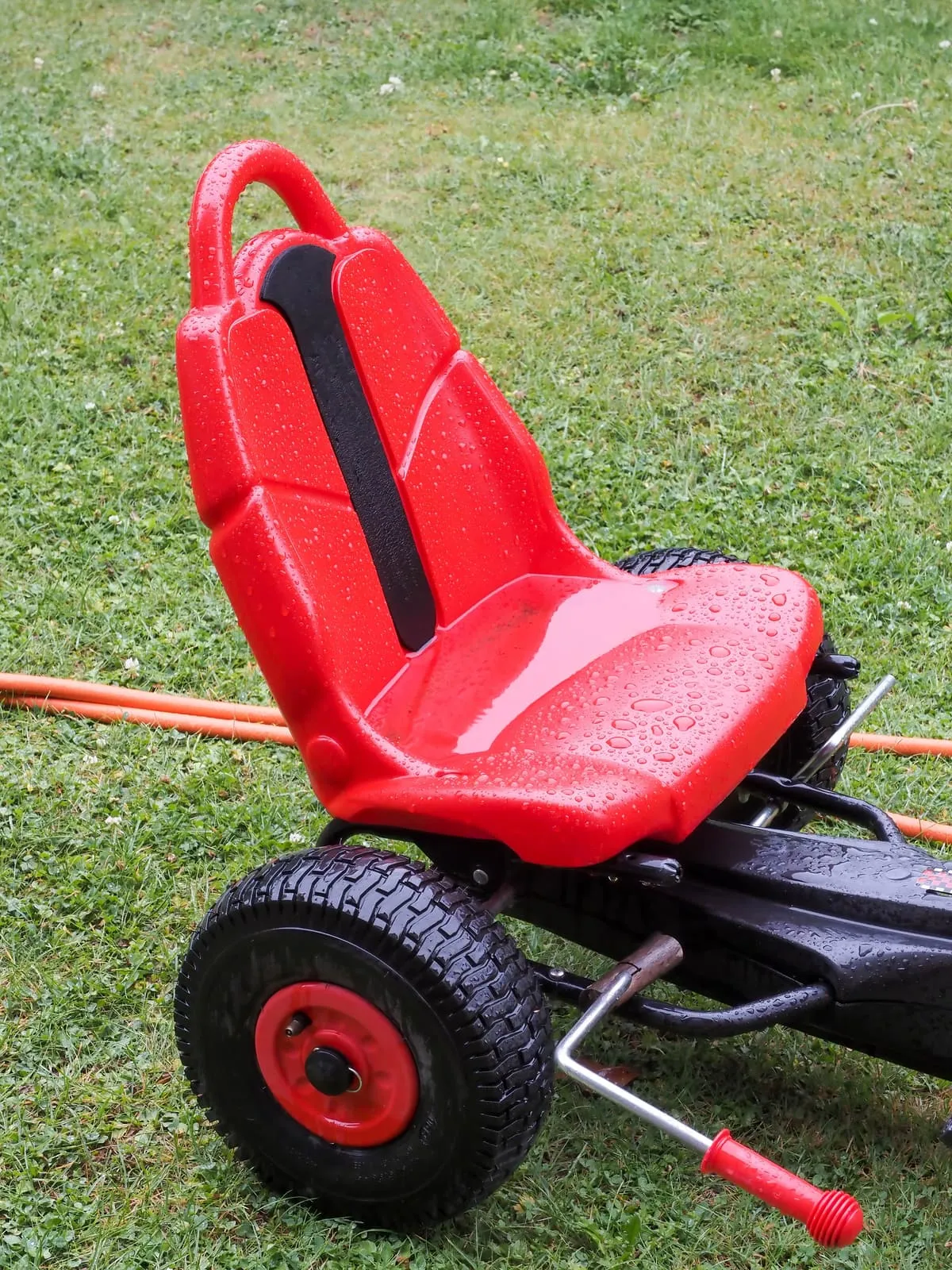 Red plastic seat of a pedal go-kart on wet grass, 2020