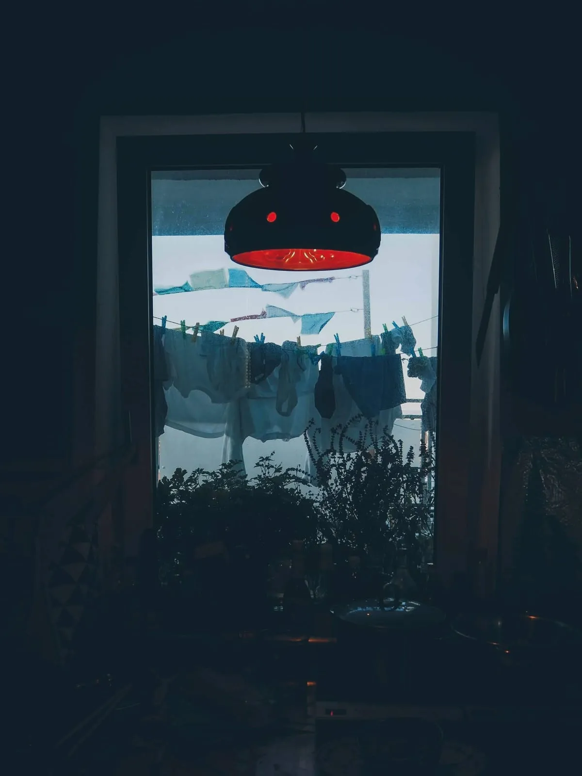 Dark room, a red lamp against a window with hanging laundry