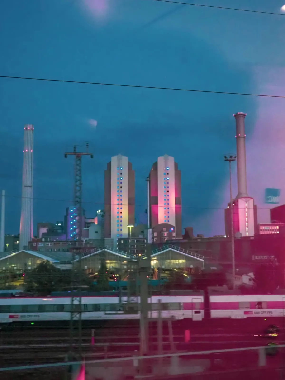 Power plant towers lit pink behind railway lines at dusk, 2020