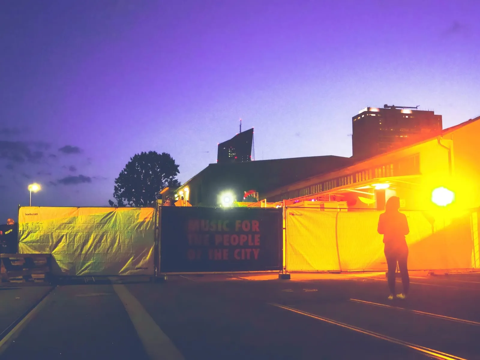 Figure in orange light beside a lit construction fence at dusk