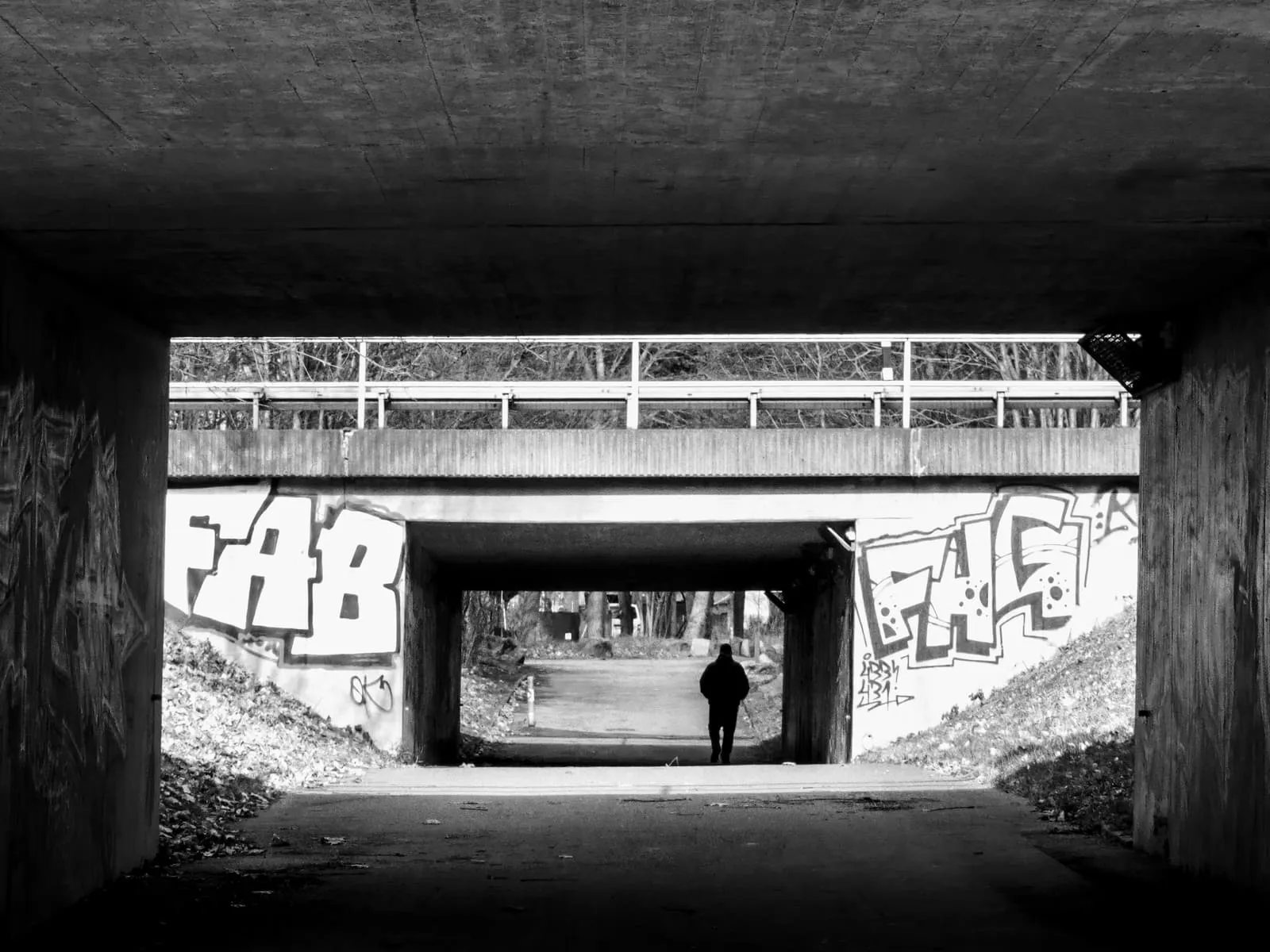 Black and white underpass framing a second bridge and a lone walker, 2020