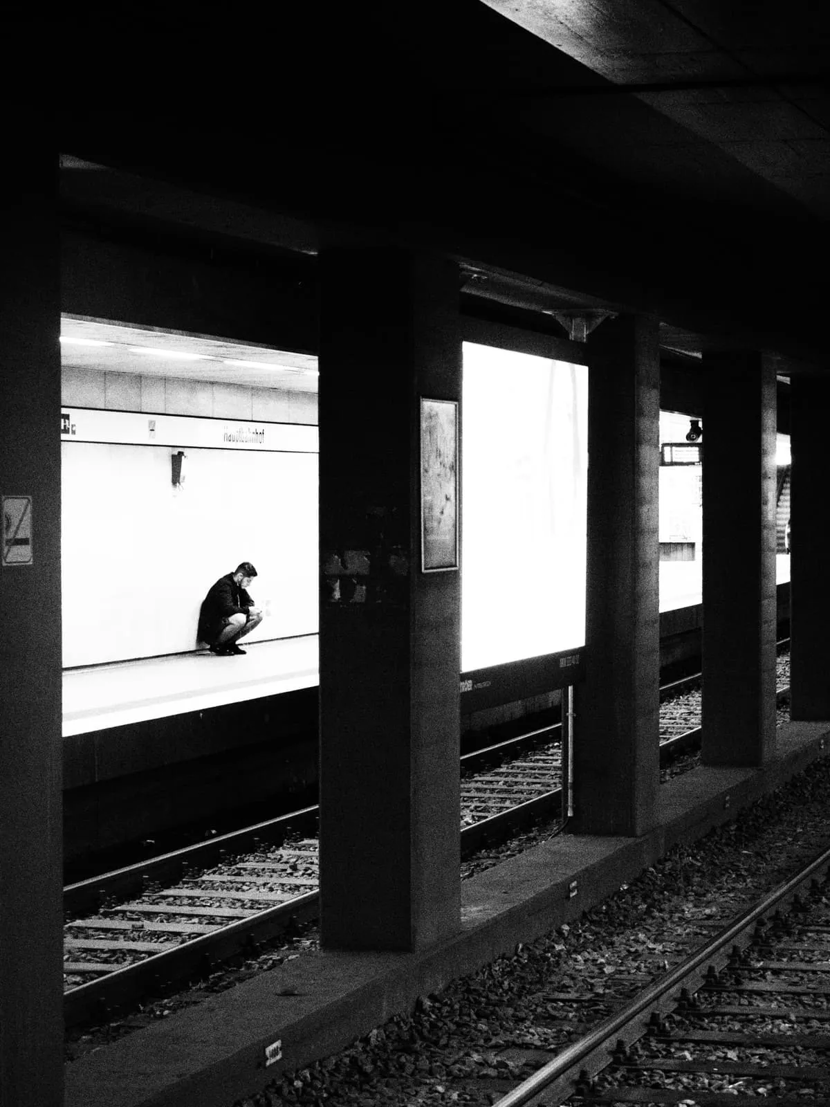 Black and white platform, one figure crouching in a bright opening, 2021
