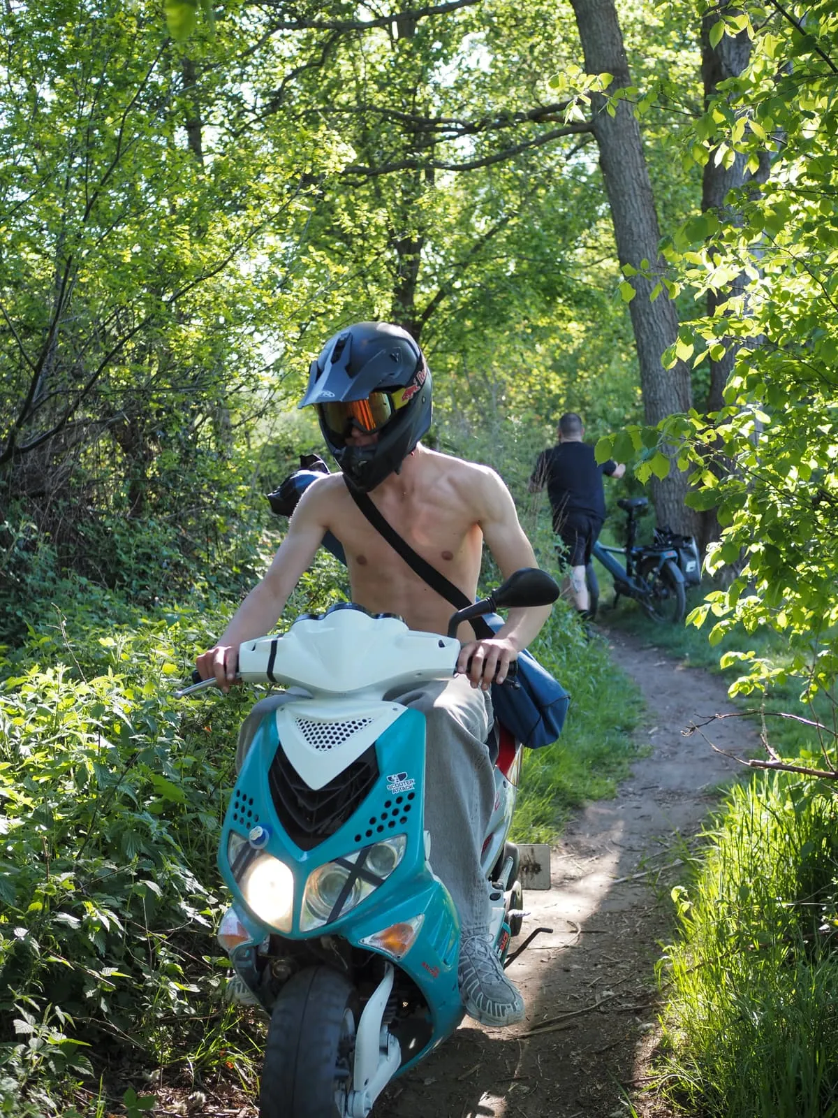 Shirtless rider in a full helmet on a scooter on a forest path, 2026