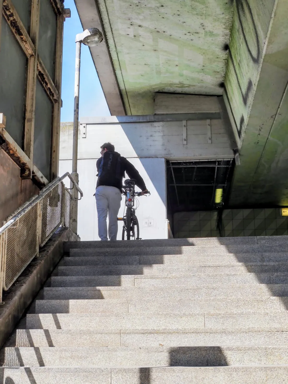 Cyclist pushing a bike up concrete steps, from behind, 2026