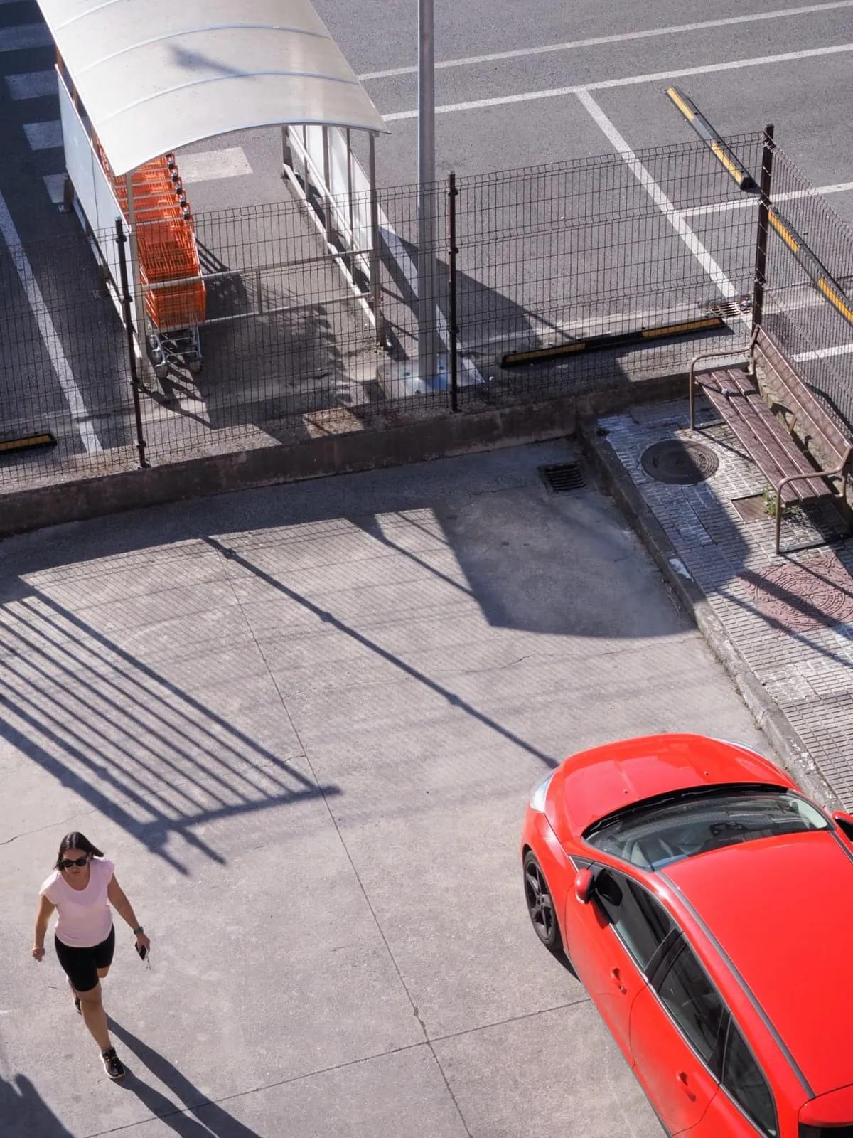 From above: a walker and a red car on a paved yard, 2024
