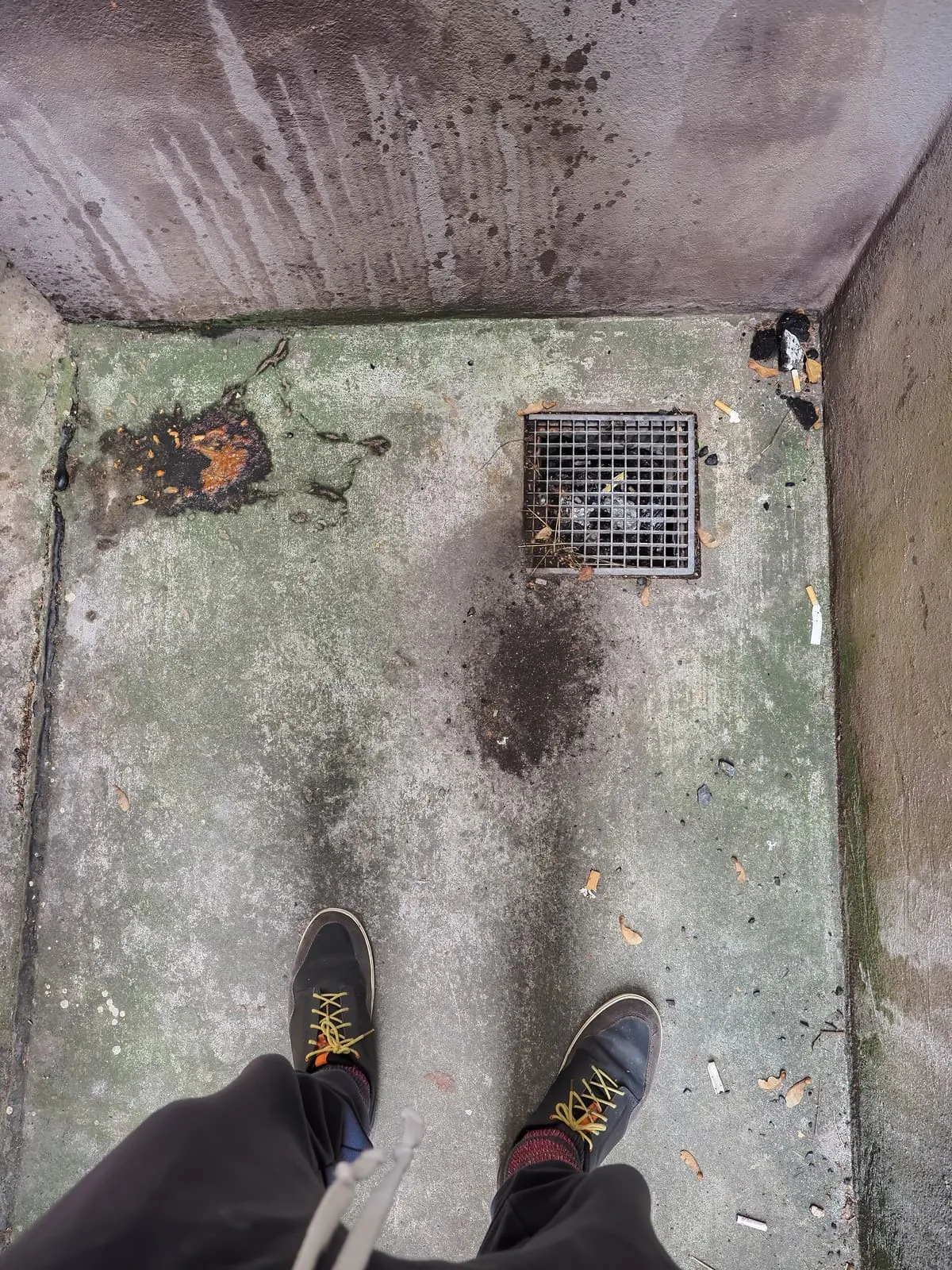 Two shoes at the edge of a stained concrete pit with a drain, 2020
