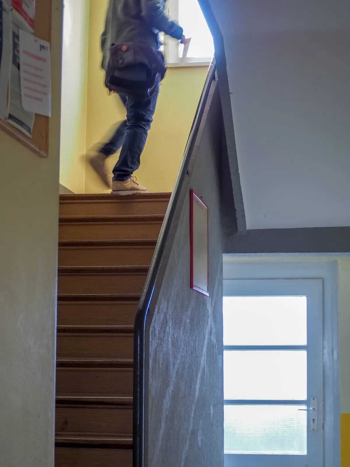 Legs climbing a wooden stair past a yellow wall, a door below, 2020