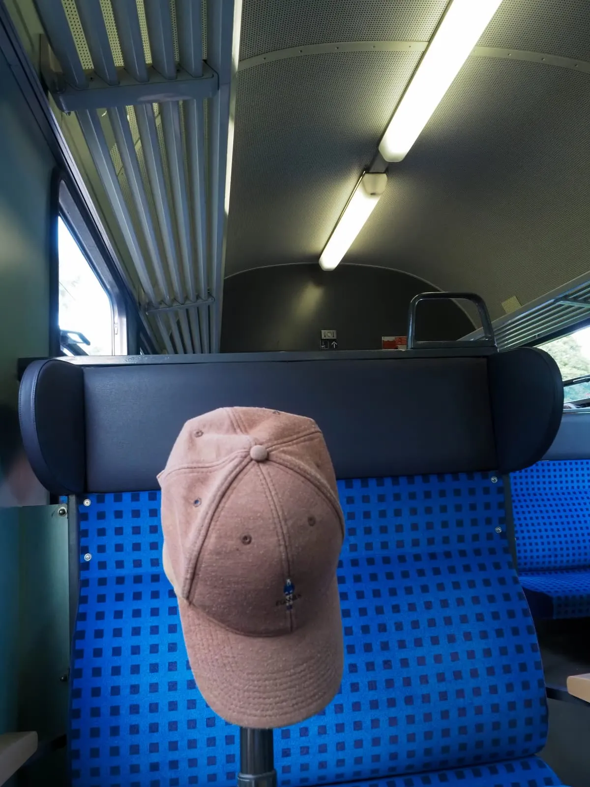 A brown cap hung on the headrest of an empty train seat, 2020