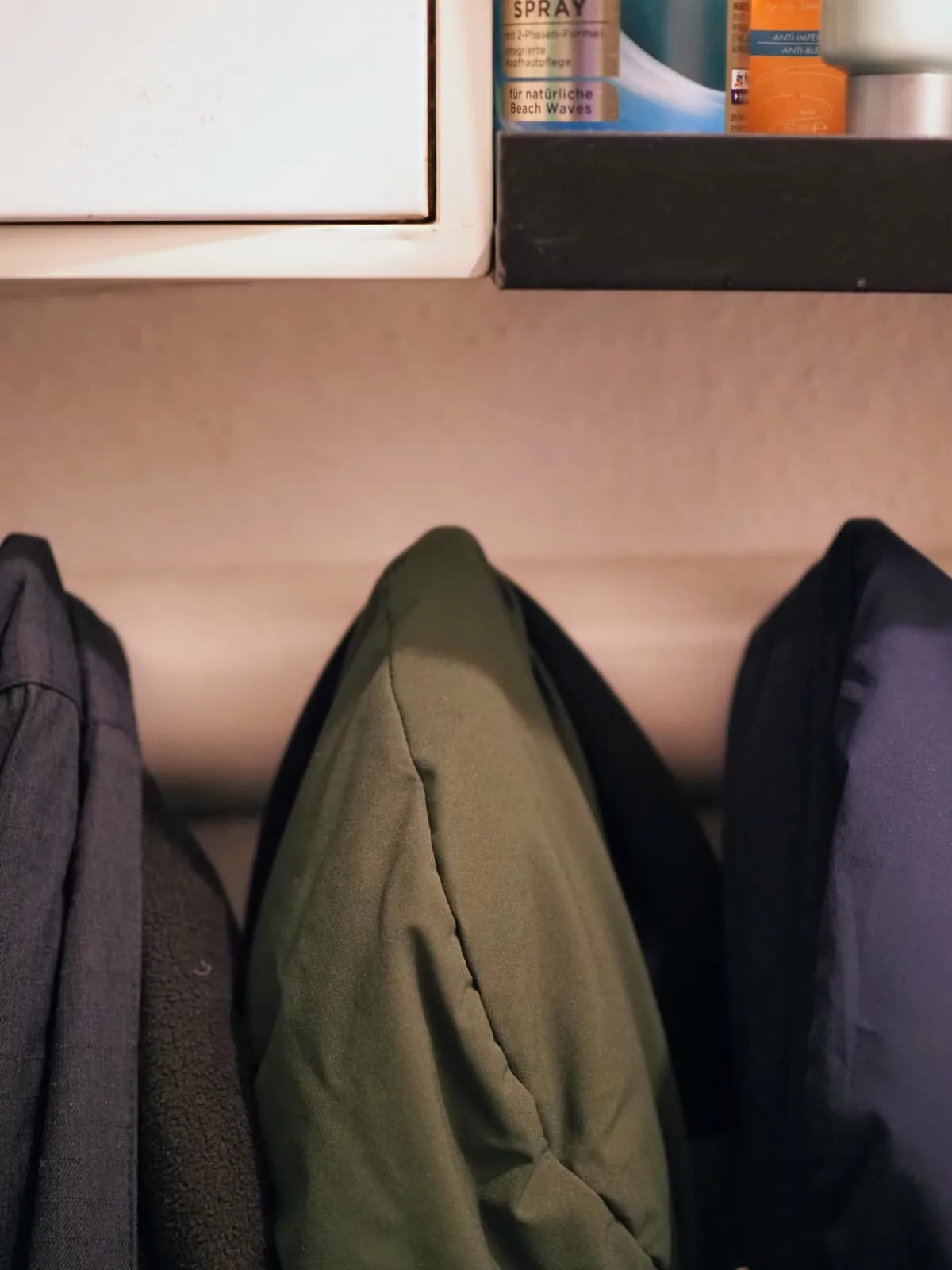 Three jackets on hooks under a bathroom shelf, 2025