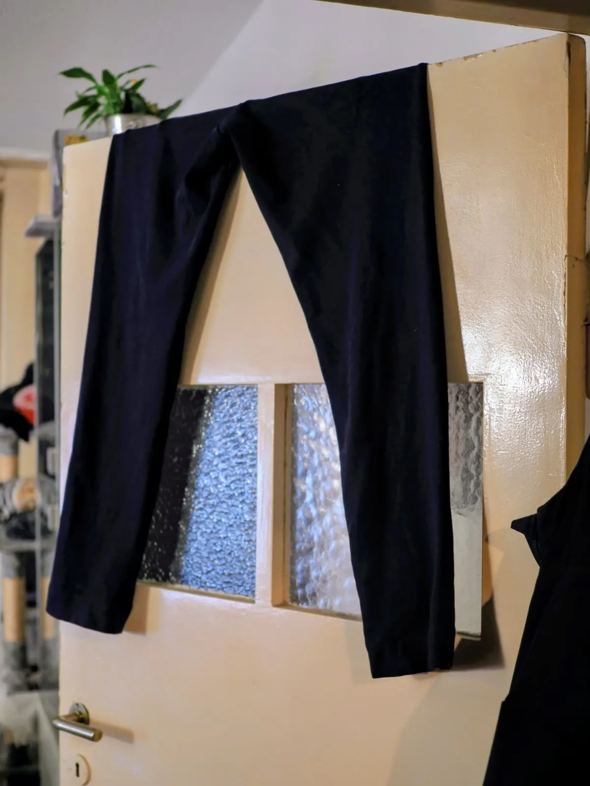 A pair of black trousers hung over the top of a door, 2025