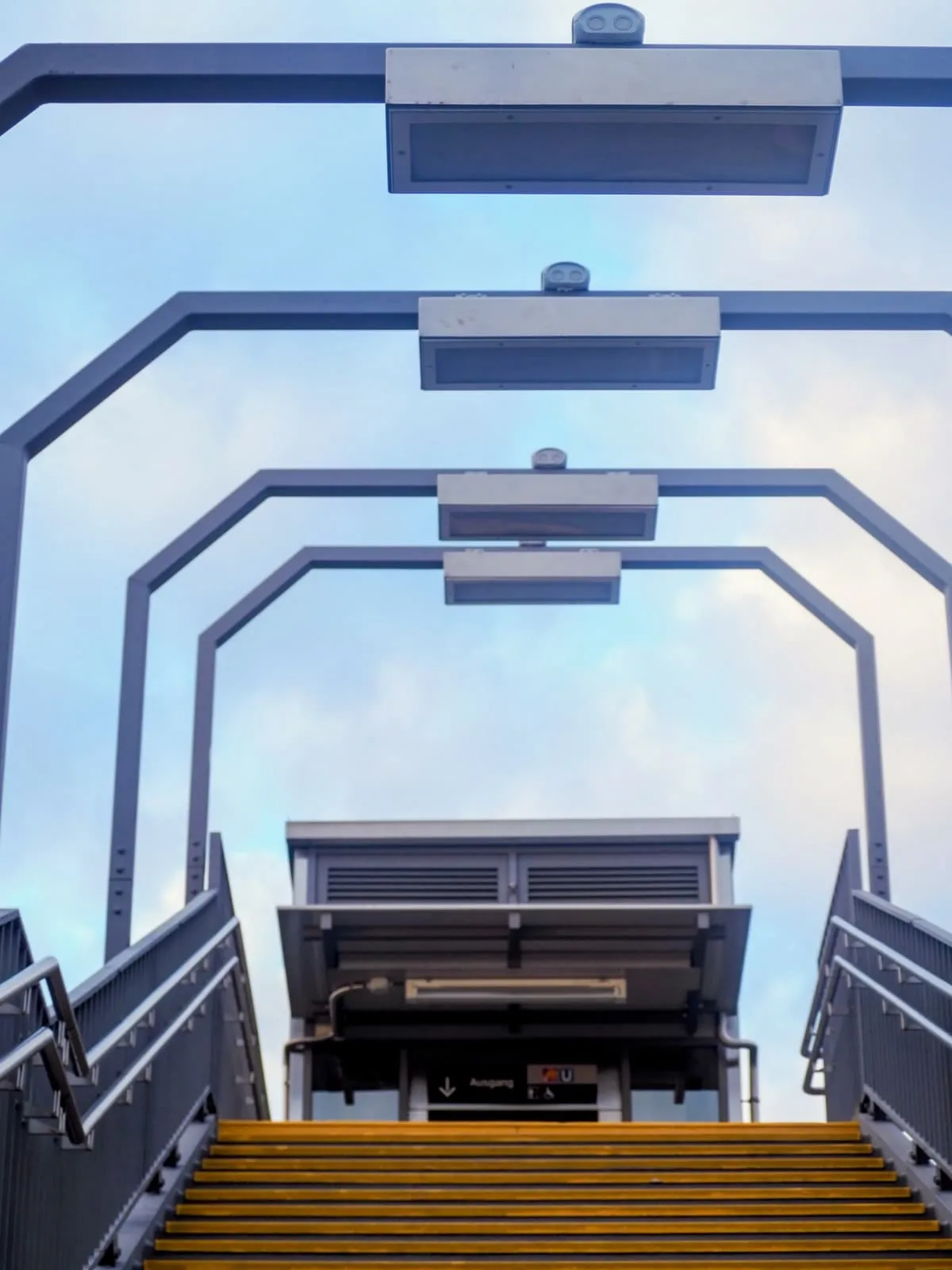Yellow steps up to a platform under grey steel arches, 2025