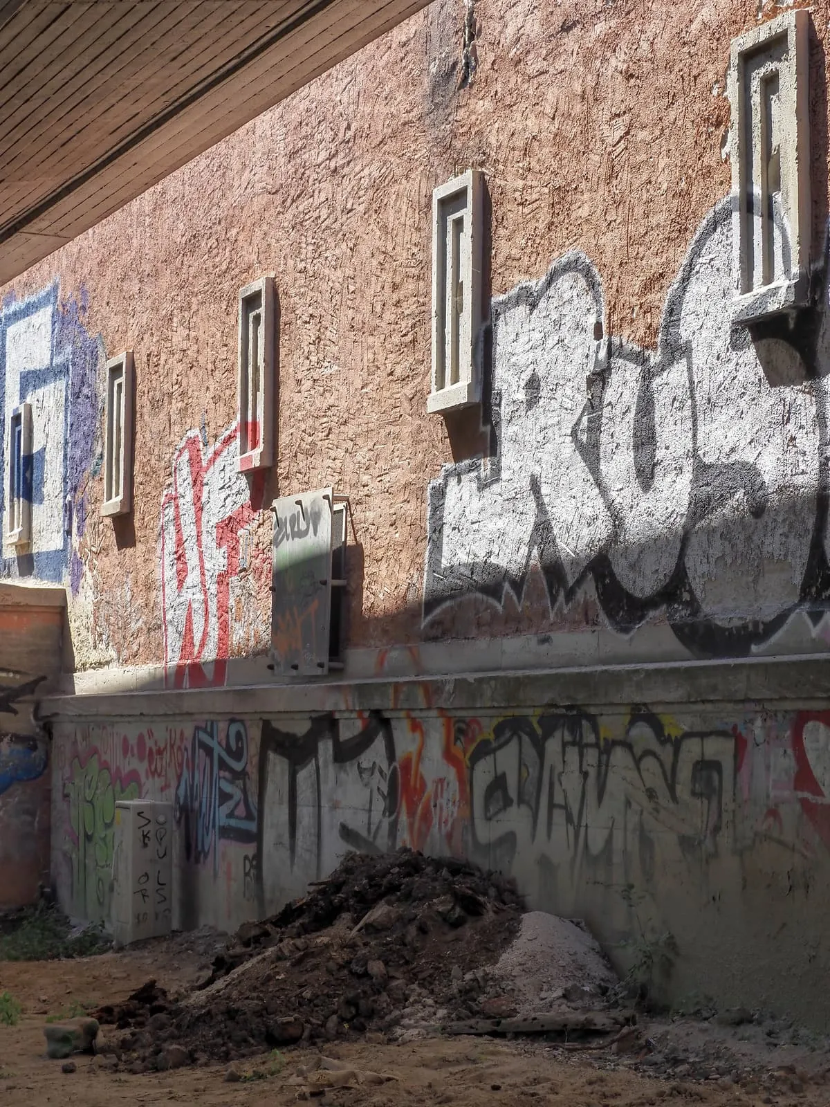 Brick wall with graffiti and small windows, a pile of earth, 2020