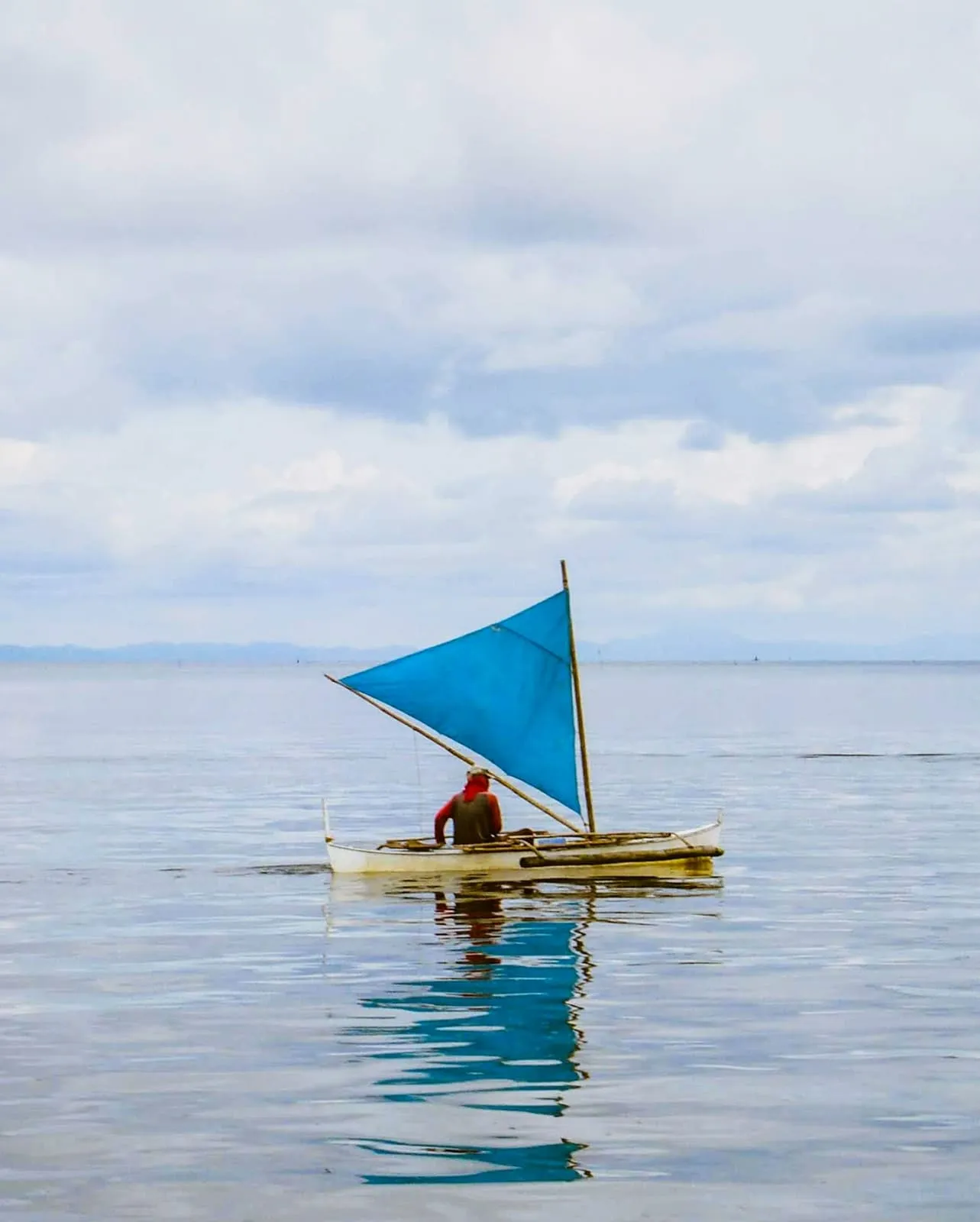 Small boat with a blue sail on a flat sea