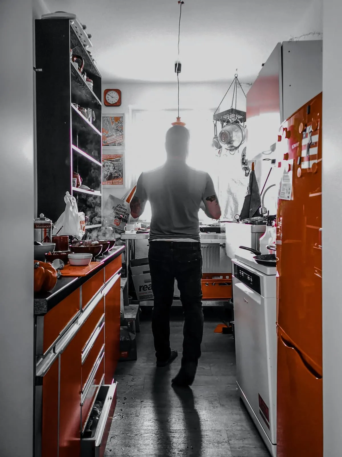 Man from behind in a narrow kitchen with orange cabinets, 2019