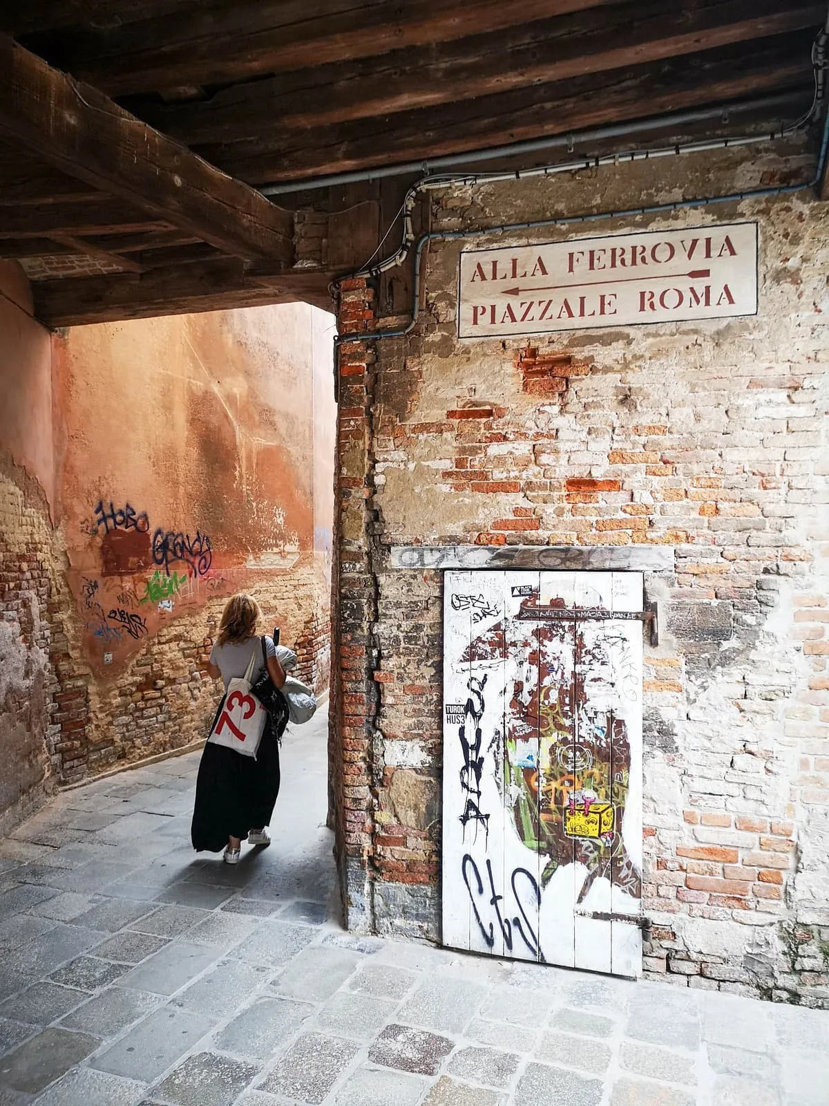 Woman walking away through a brick passage under street signs, 2019, Venezia
