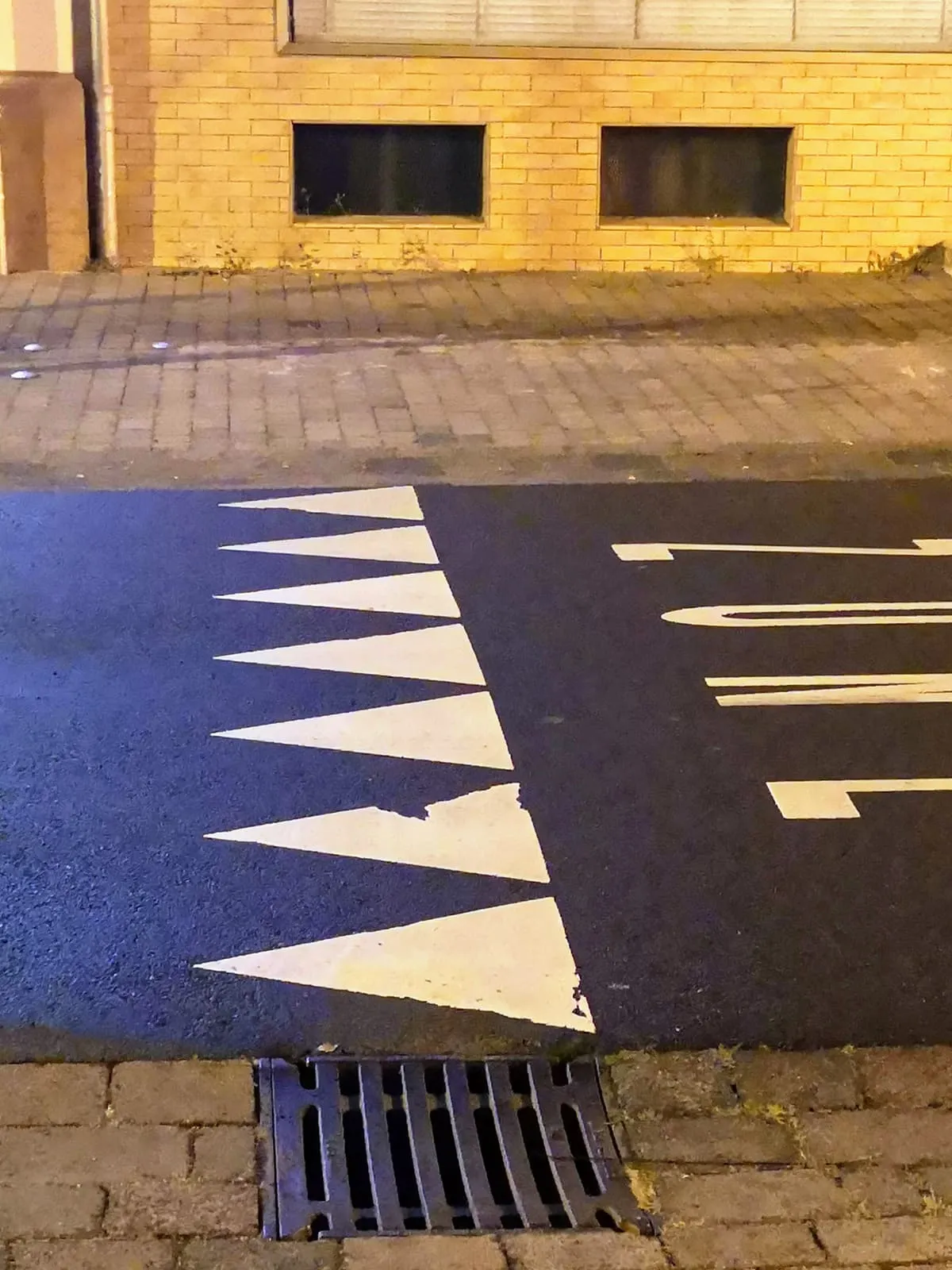 White triangles painted on blue asphalt before a yellow wall, 2019