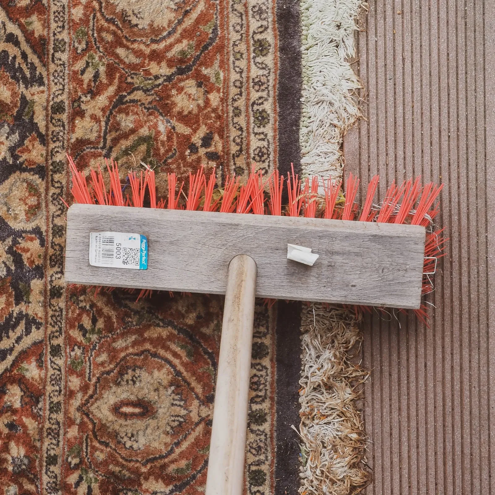 Broom with red bristles lying on a patterned carpet, 2020